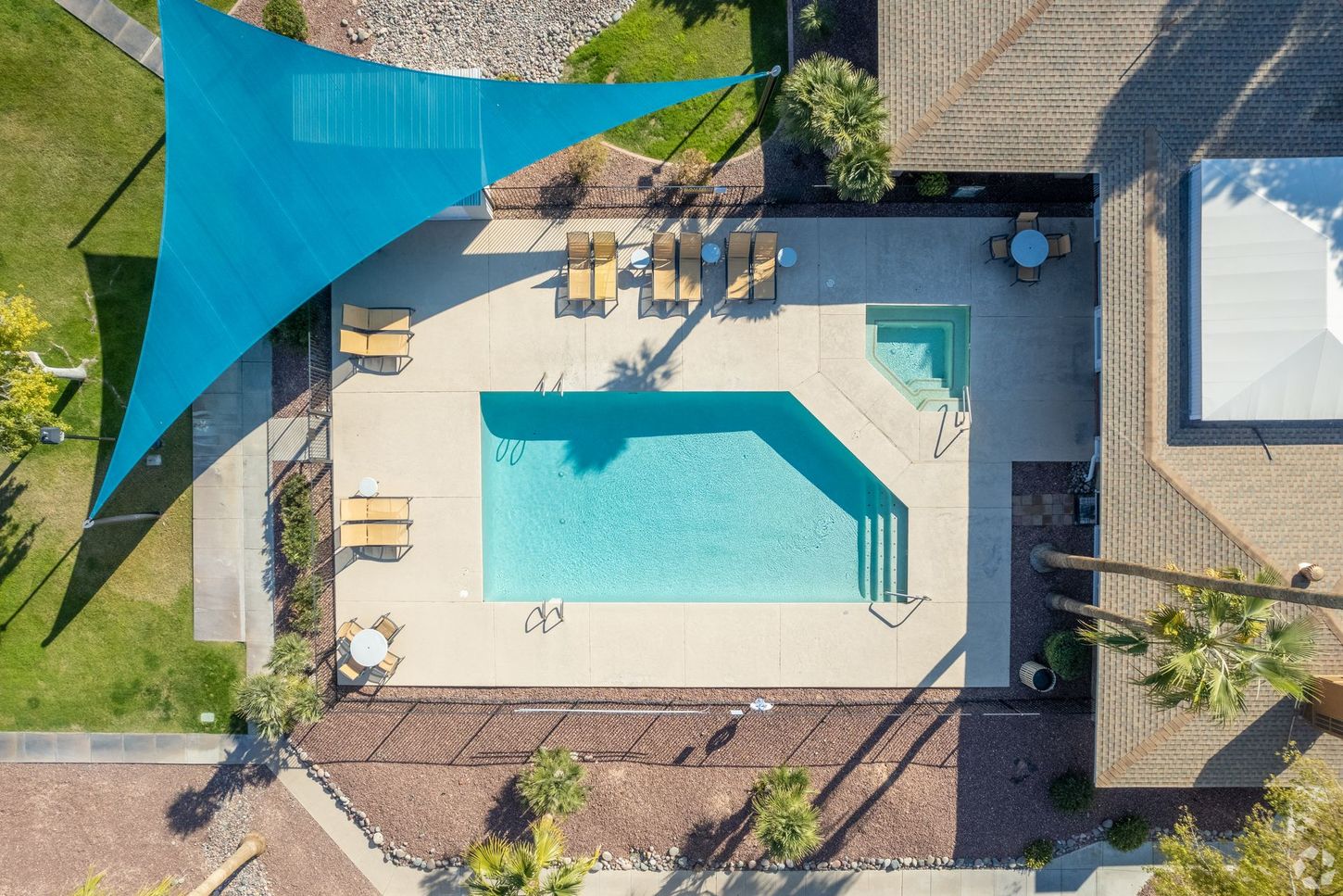 Overhead view of a swimming pool with a blue shade sail and lounge chairs.
