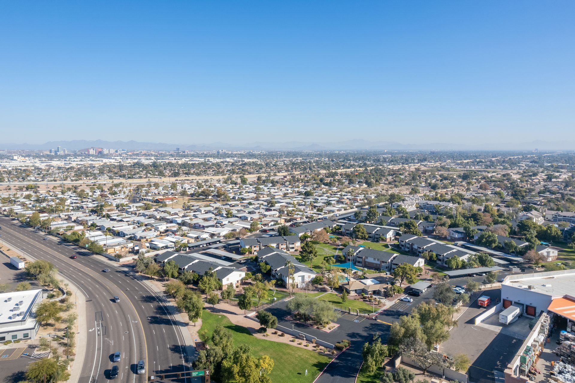 Aerial view of a suburban neighborhood with roads, houses, and businesses under a clear blue sky.