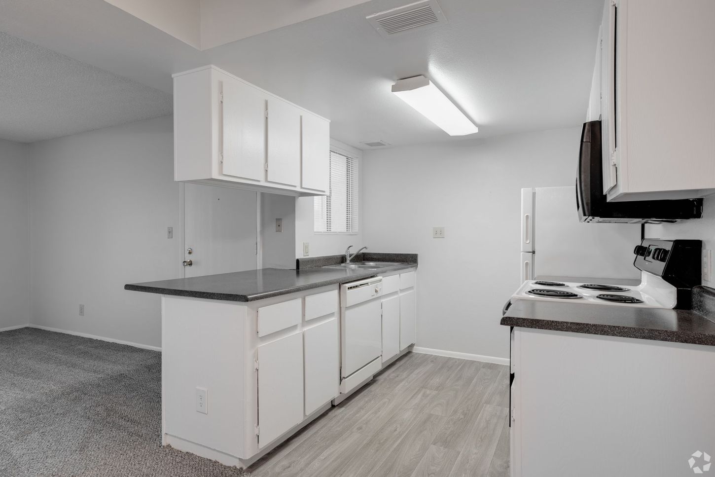 Kitchen with white cabinets, dark countertops, and a white appliance. Gray flooring.