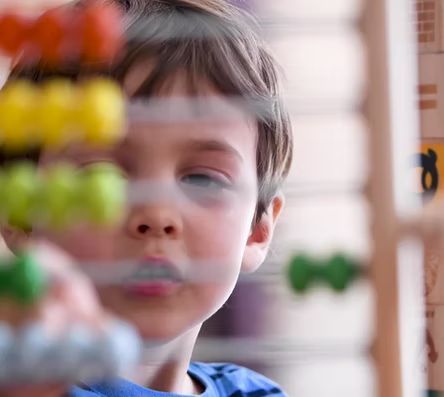A young boy is playing with a wooden bead maze.