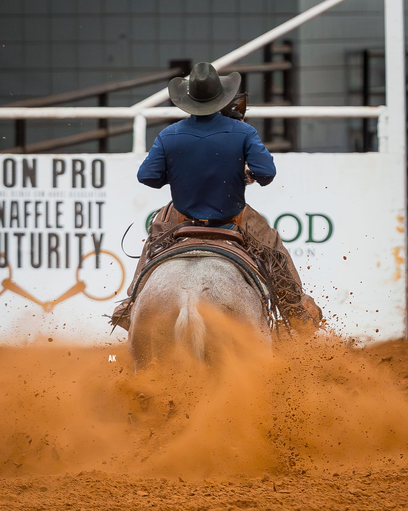 A cowboy on a brown horse sliding in sand during a reining competition; they're in a dirt arena.