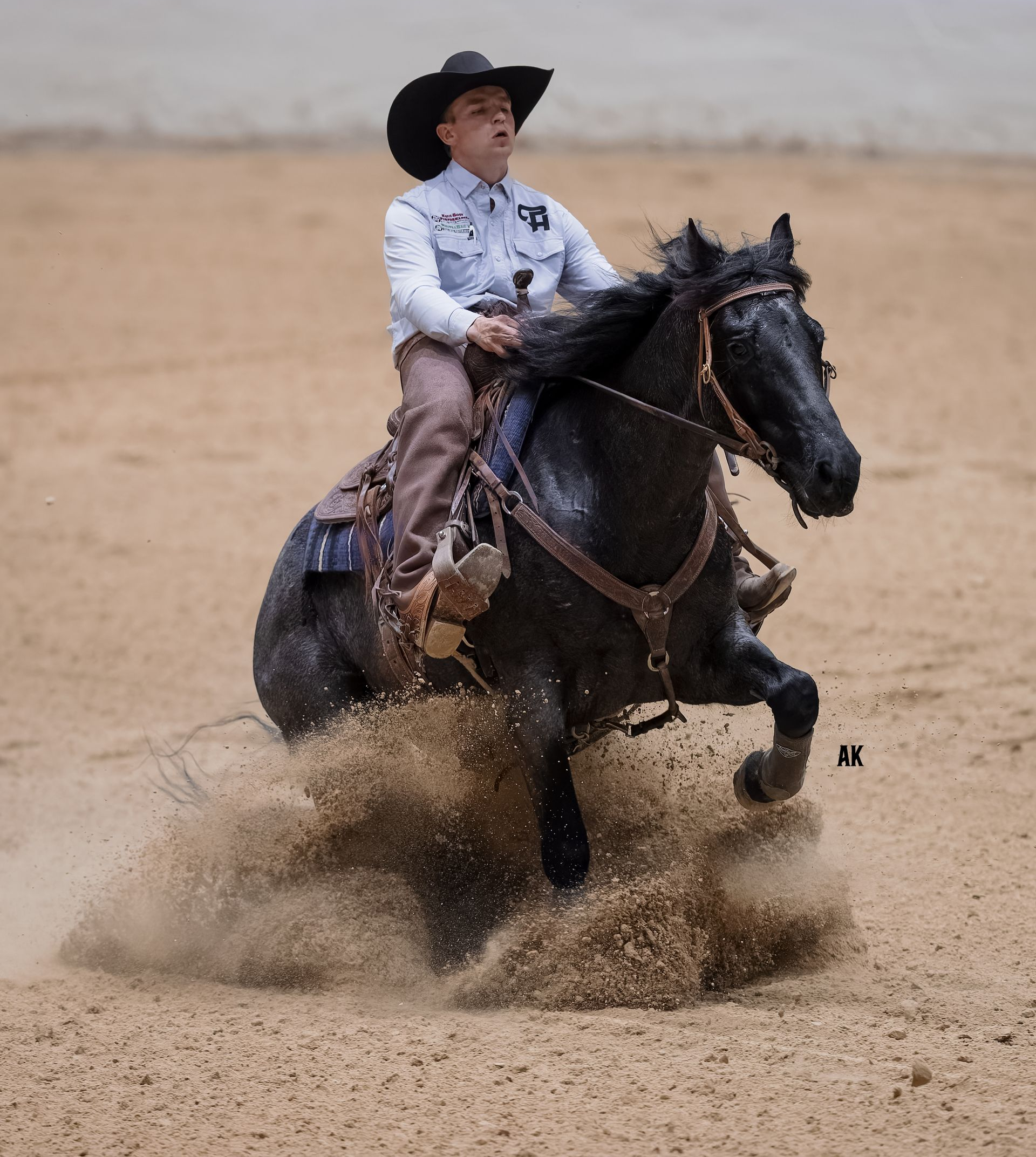 Man on gray horse in arena, performing a reining maneuver.