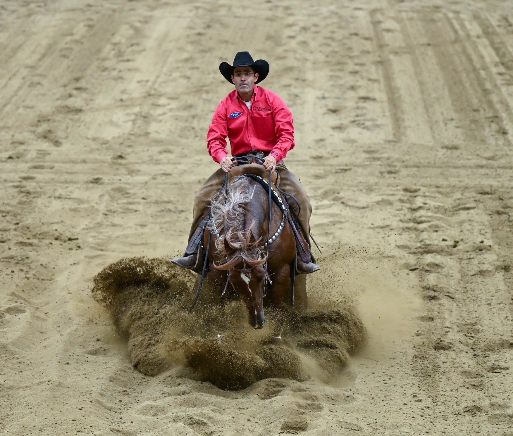 Cowboy on horse slides through dirt in a competition arena.