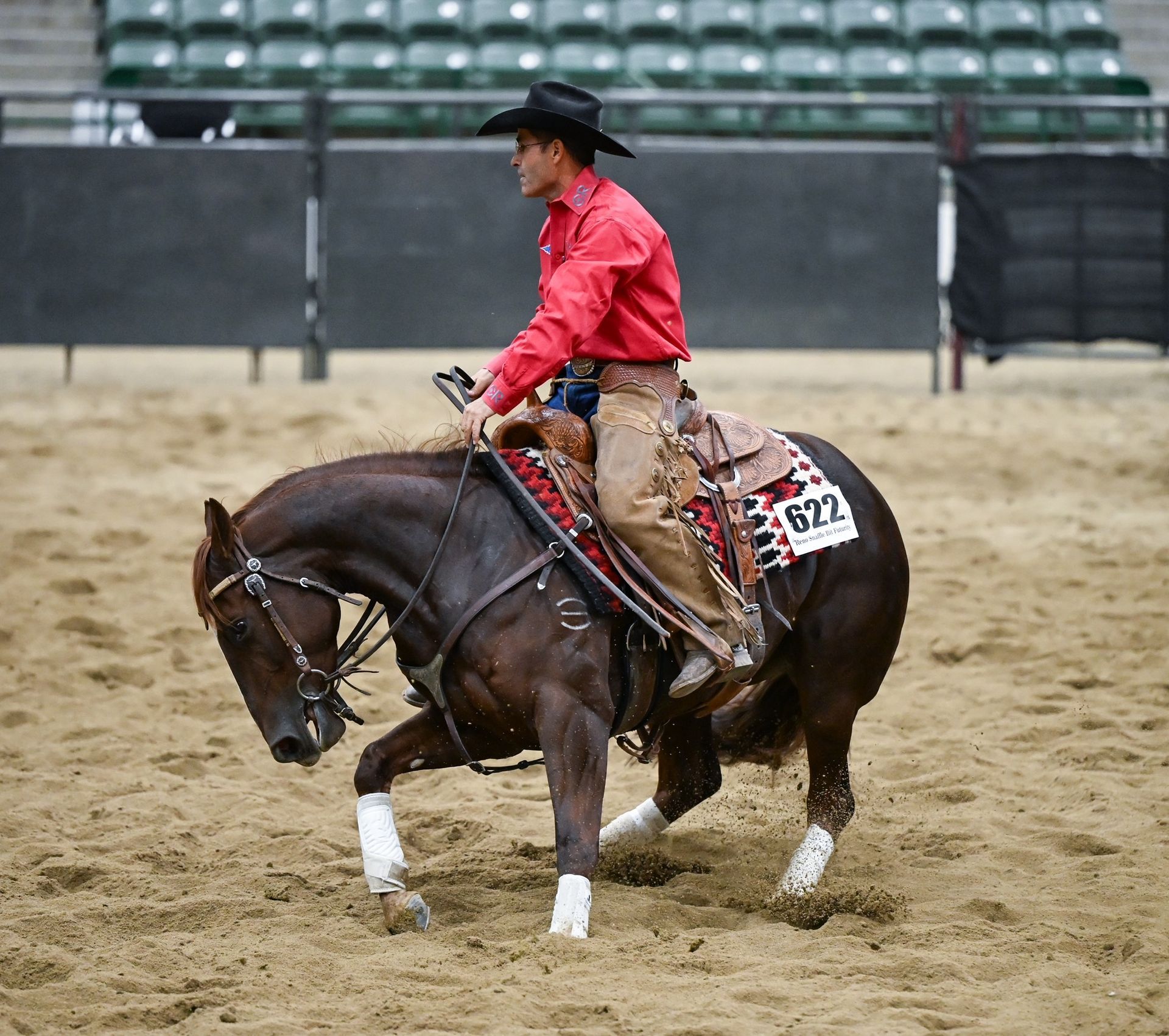 Cowboy on horse performing a reining spin in a competition arena.
