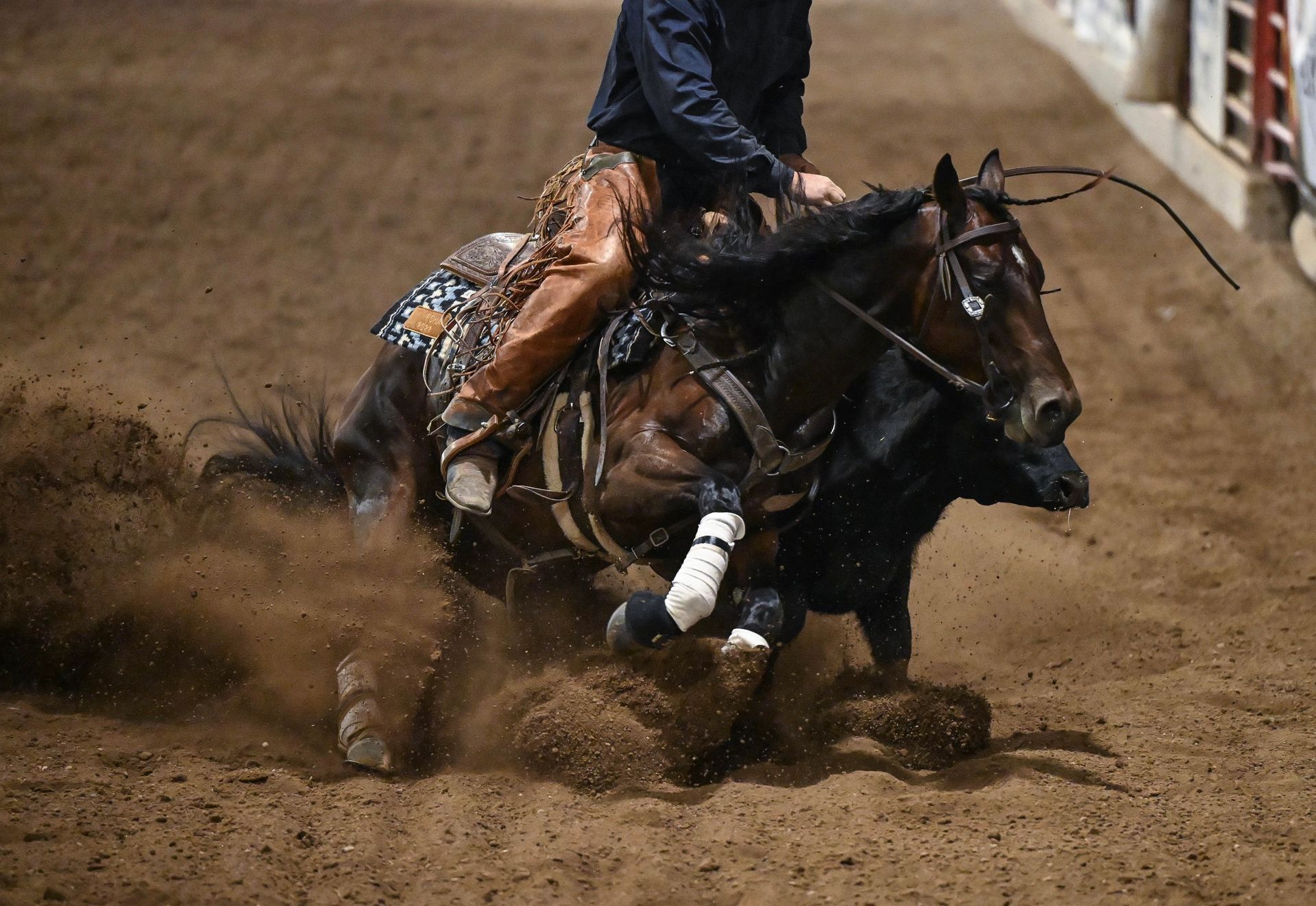 A cowboy on horseback cuts a steer in a dusty arena.