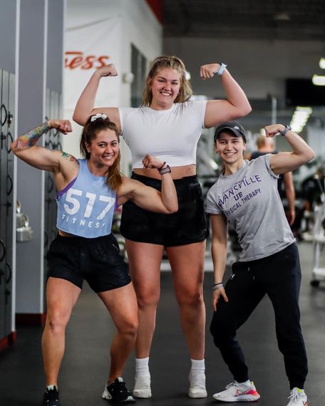 three women are posing for a picture in a gym while flexing their muscles .