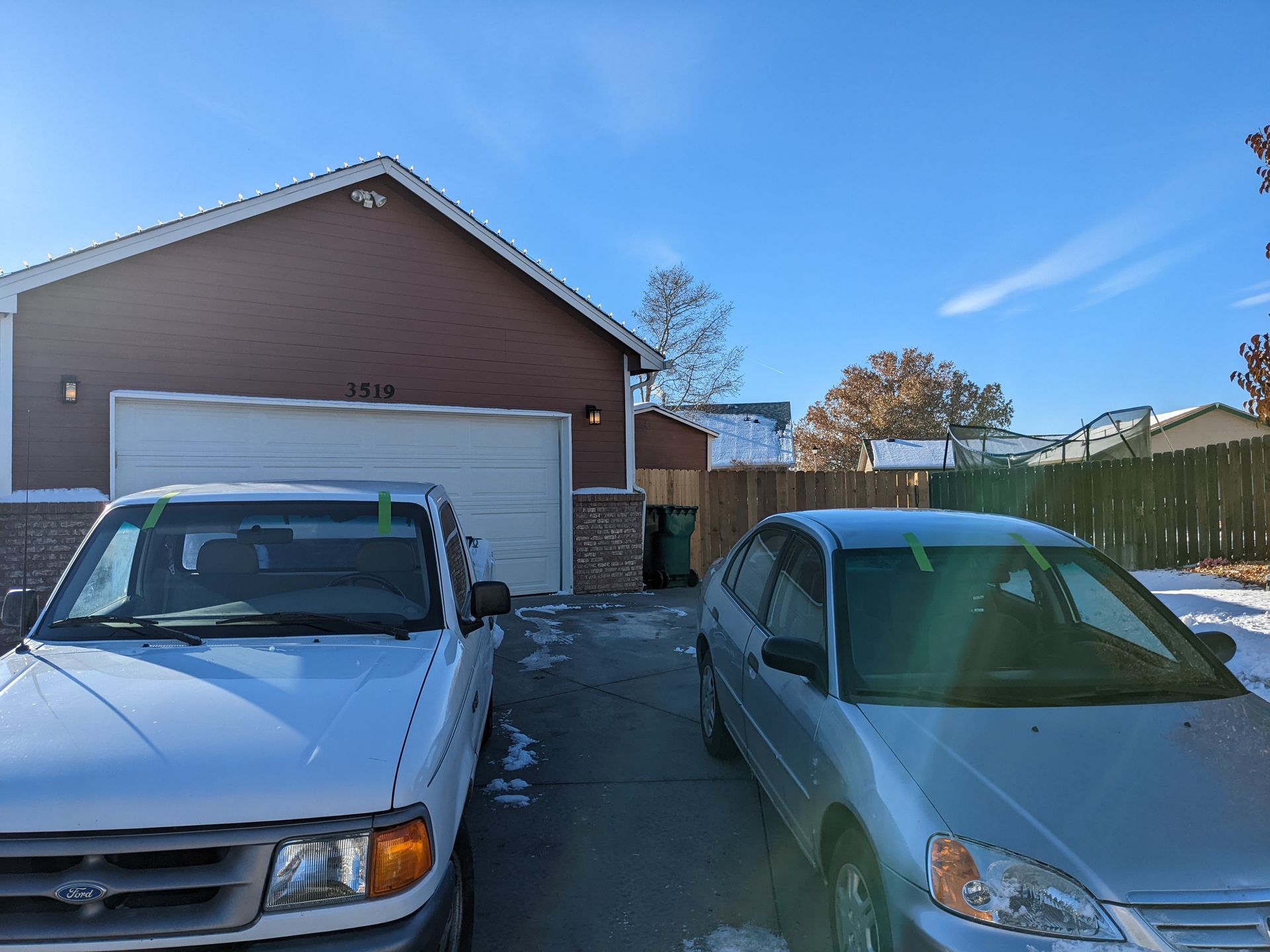 A white truck and a silver car are parked in front of a garage.