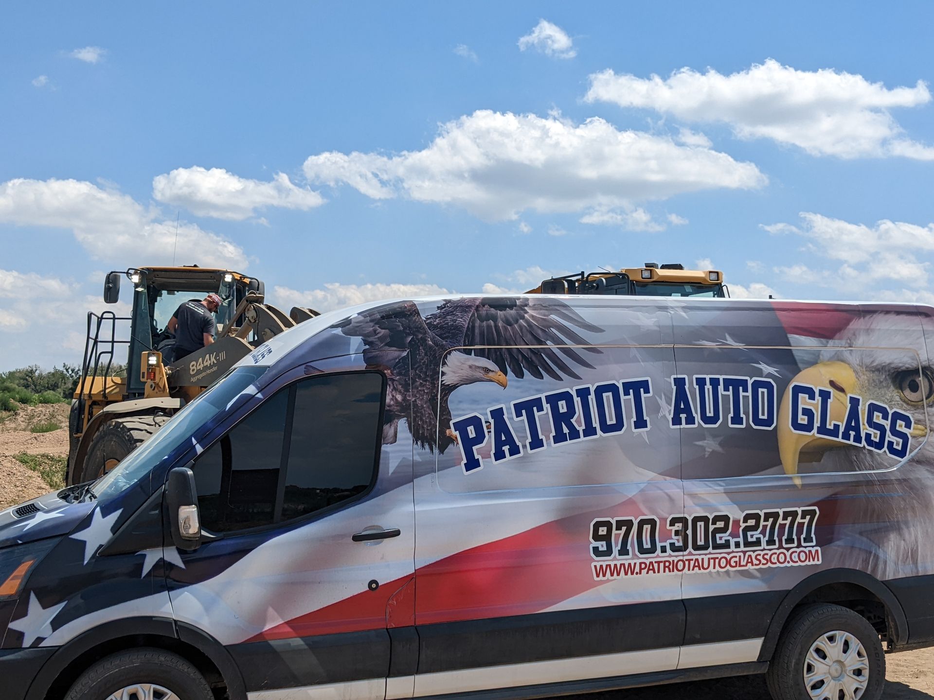 A patriot auto glass van is parked in front of a bulldozer.