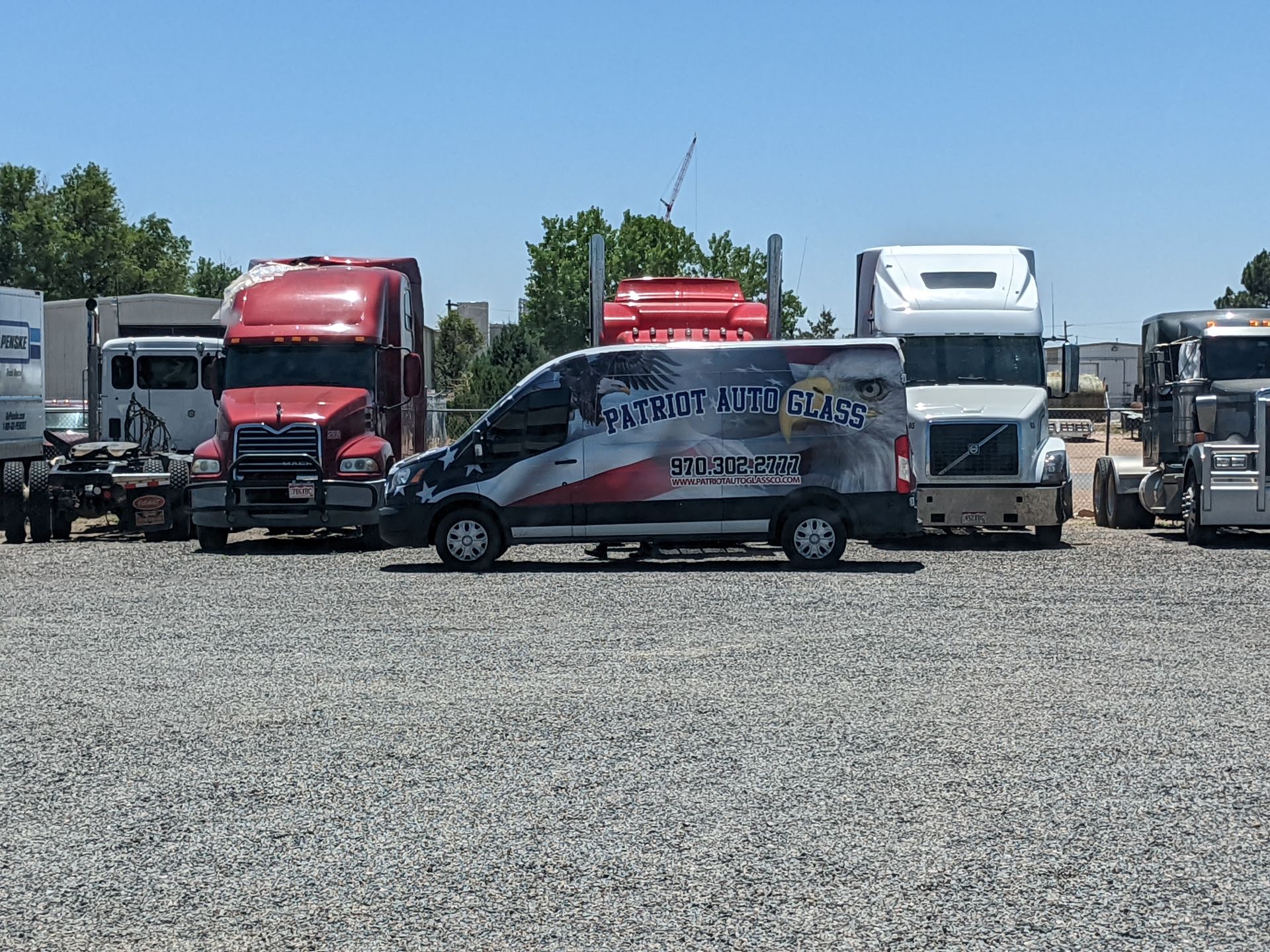 A van is parked in a gravel lot next to a row of semi trucks.