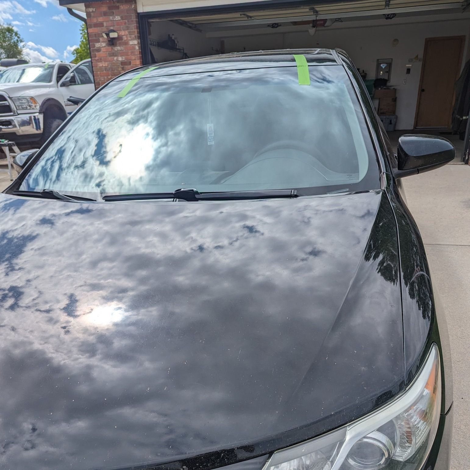 A black car with a green sticker on the windshield is parked in a garage.