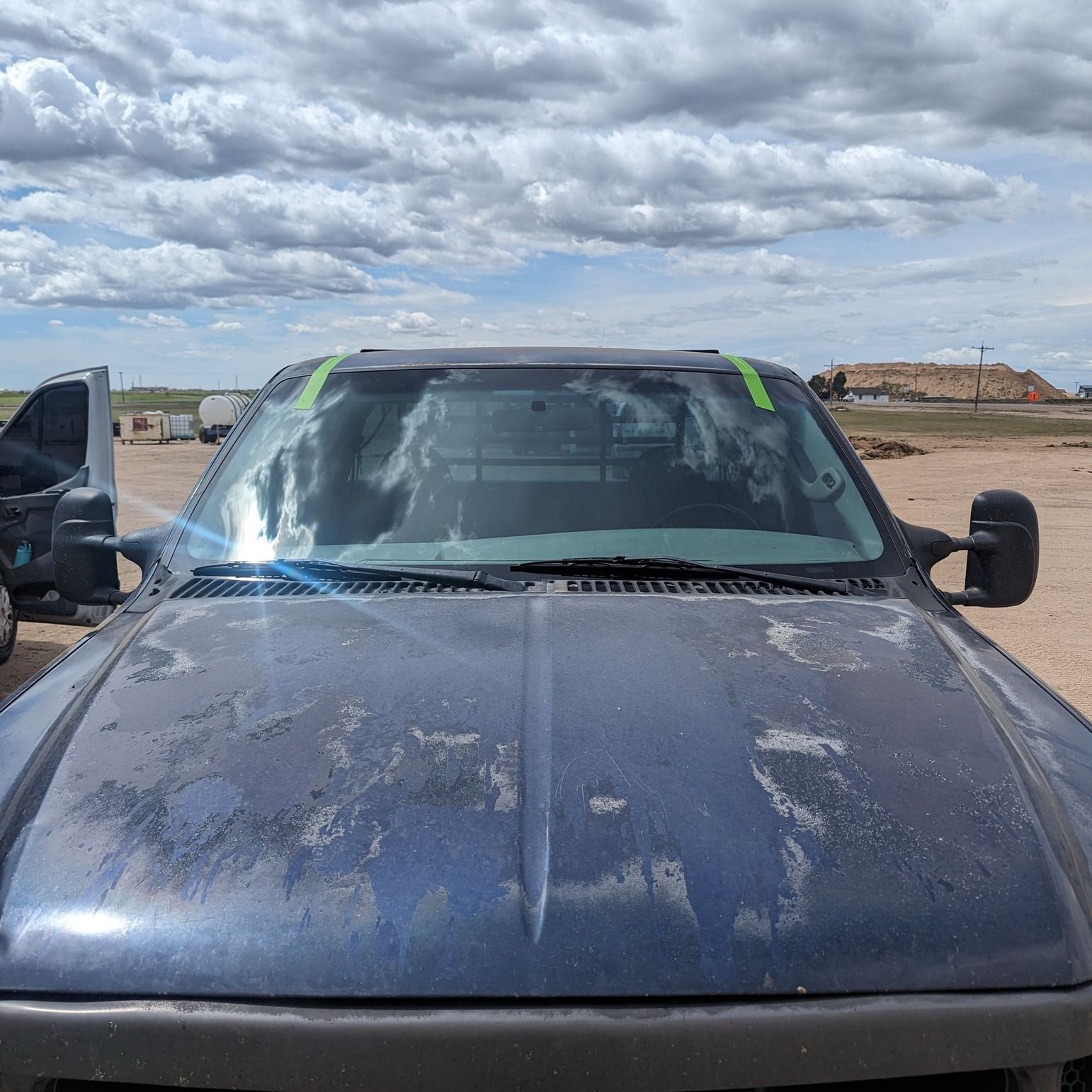 A black truck is parked in a dirt field with a cloudy sky in the background.