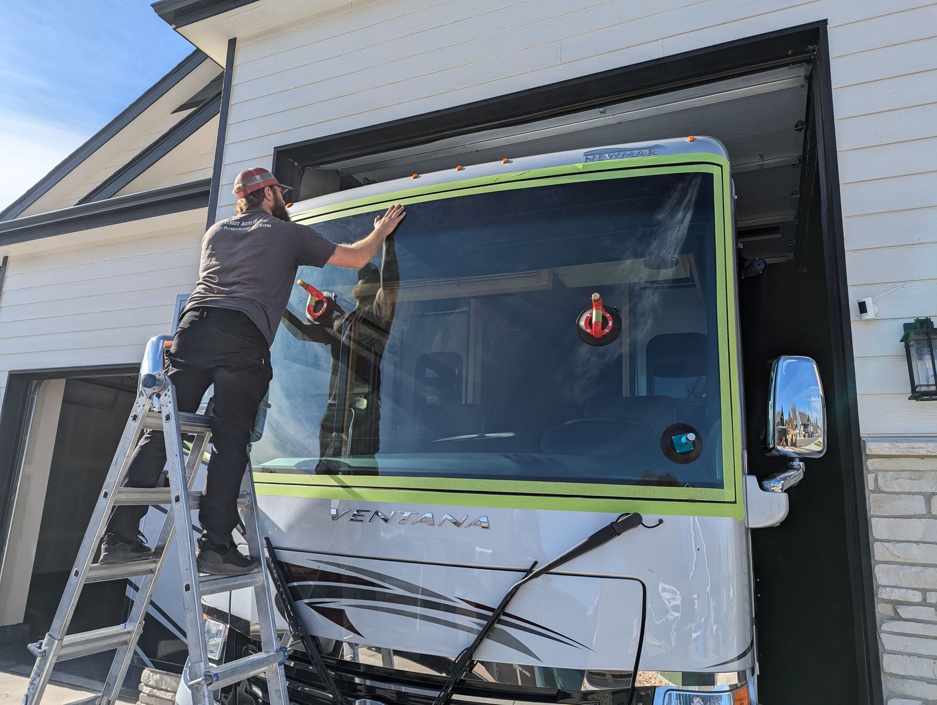A man is standing on a ladder installing a windshield on a rv.