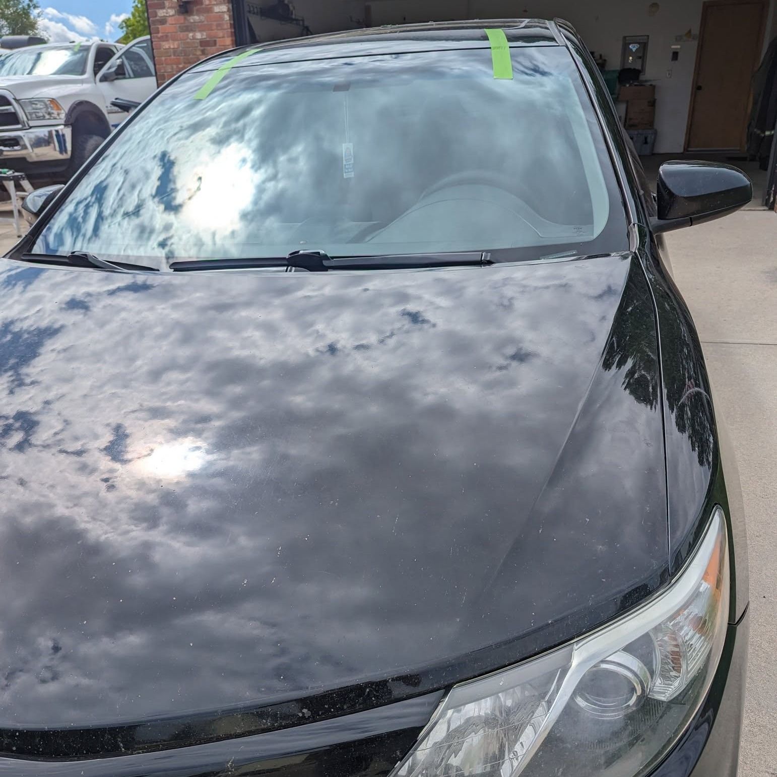 A black car with a green tape on the windshield is parked in a driveway.