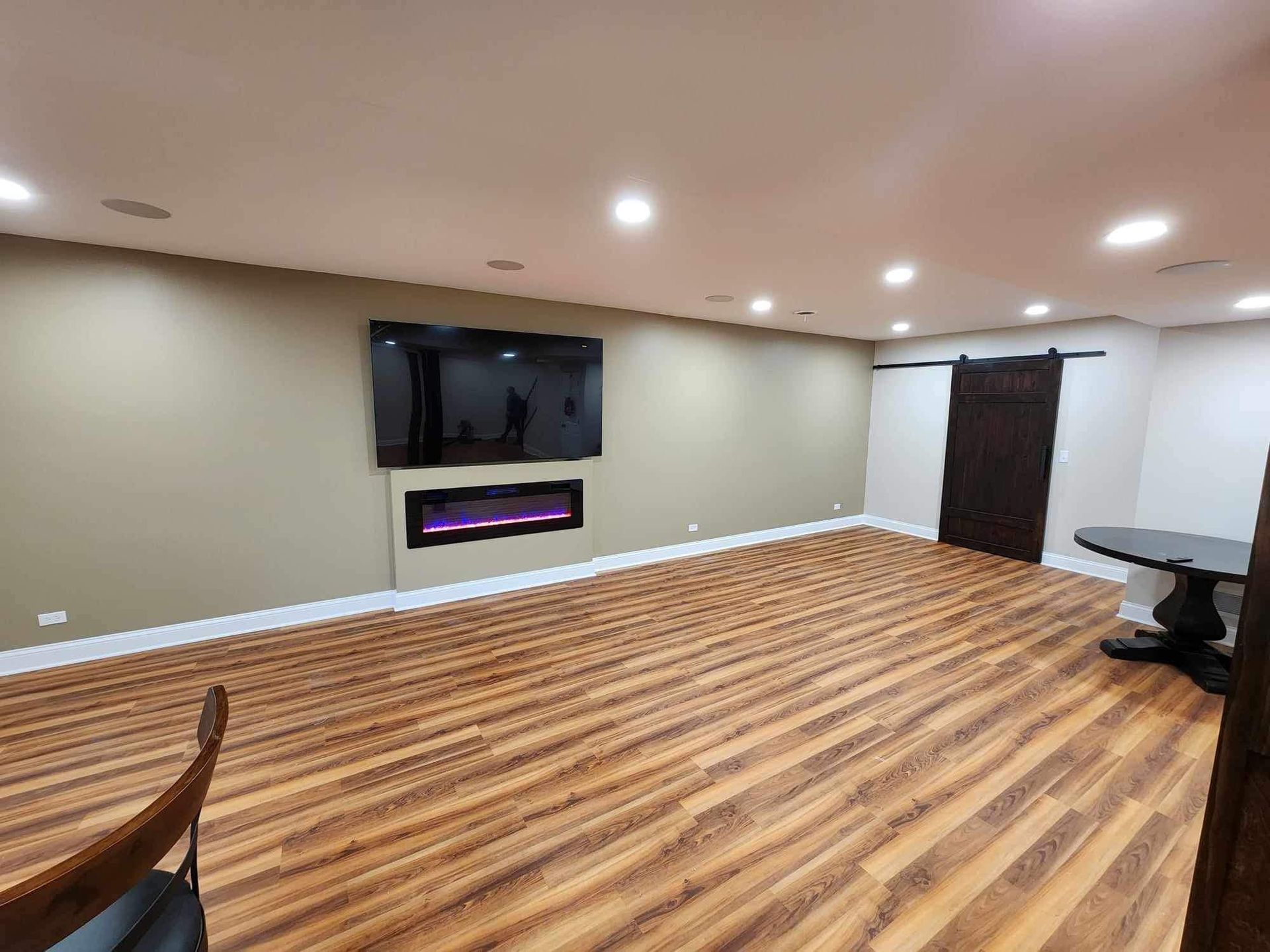 Empty basement room with wood-look flooring, wall-mounted TV, and dark double doors