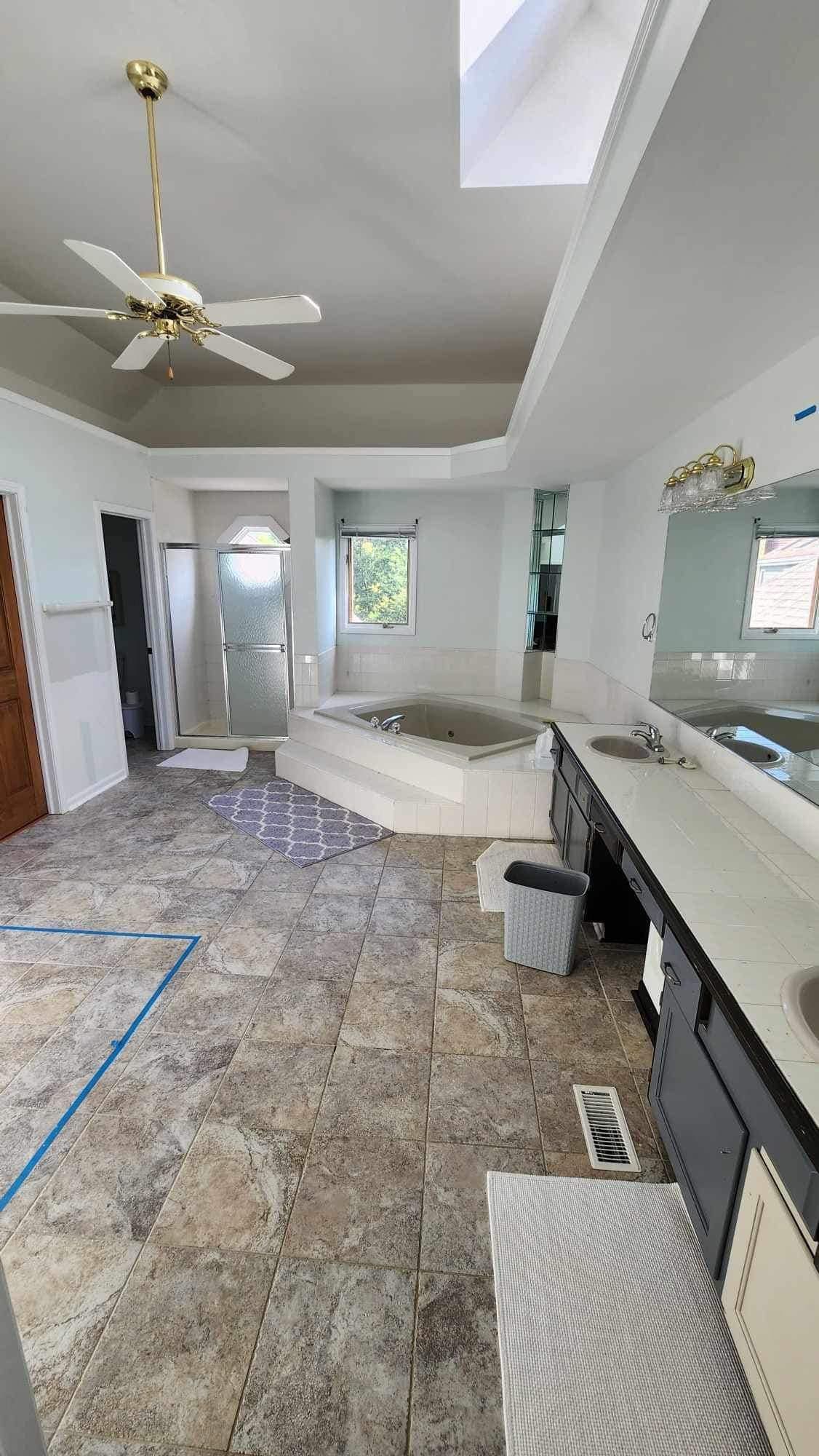 Bright bathroom with tiled floor, skylight, soaking tub, vanity, mirror, and ceiling fan