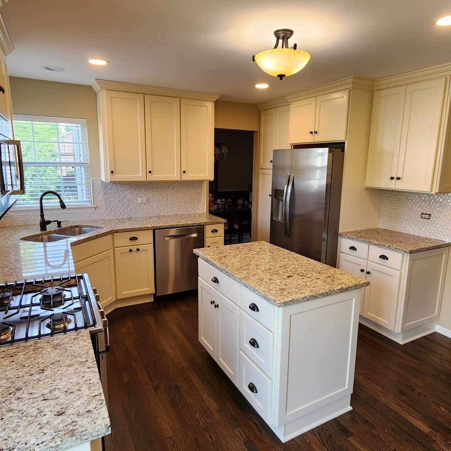 Bright kitchen with white cabinets, granite counters, stainless appliances, and a central island.