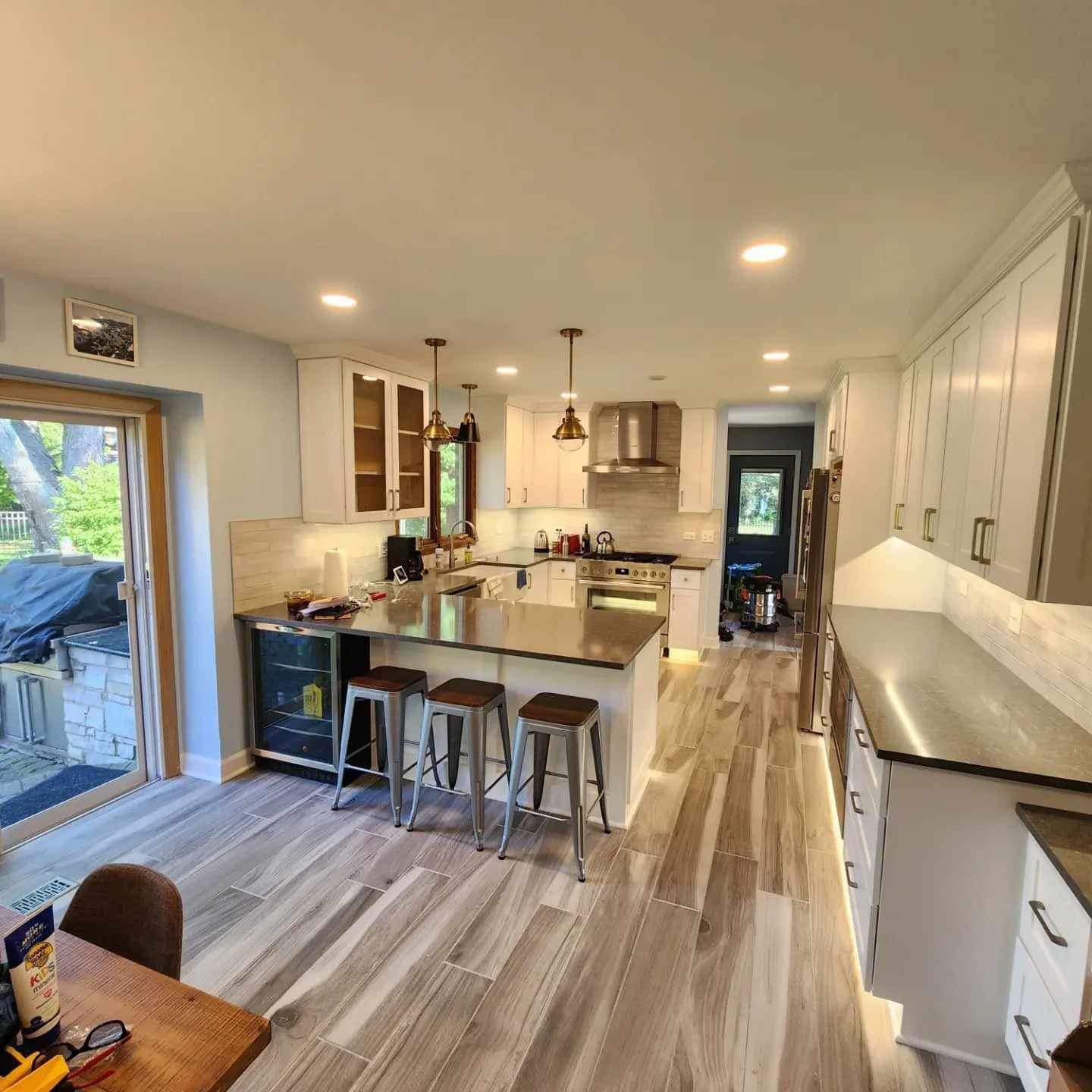A person in work coveralls and gloves installs a wooden countertop on kitchen cabinets, using a tool for measurement.