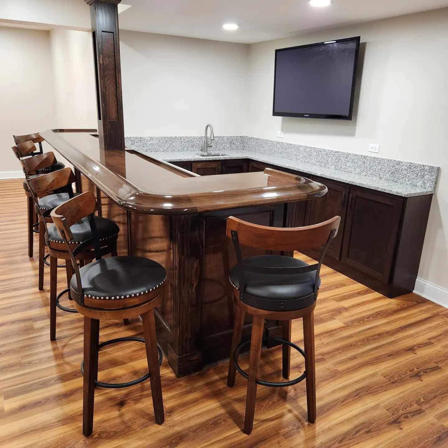 Home bar with dark wood stools, granite countertop, and wall-mounted TV in a finished basement