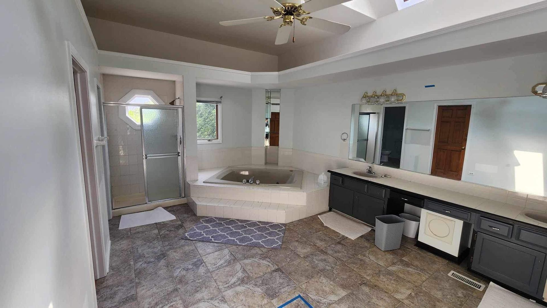 Bright bathroom with a tub, vanity, mirror, and tiled floor, viewed from the doorway.