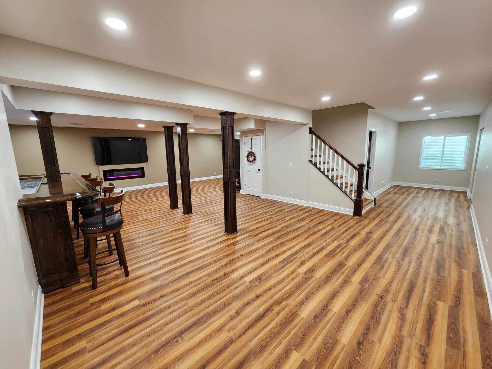 Spacious basement with wood floors, recessed lights, bar area, TV, and staircase to upper level.