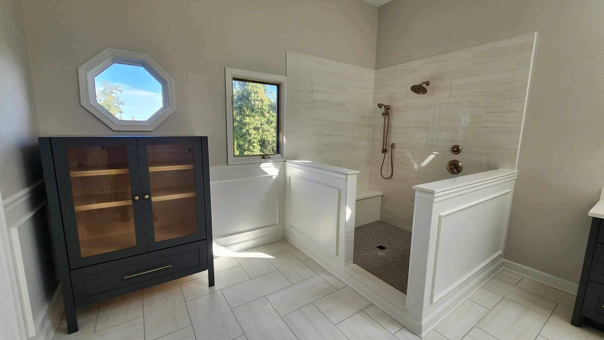 A modern bathroom with a long white double vanity, large mirror, wooden floors, freestanding tub, and black fixtures.