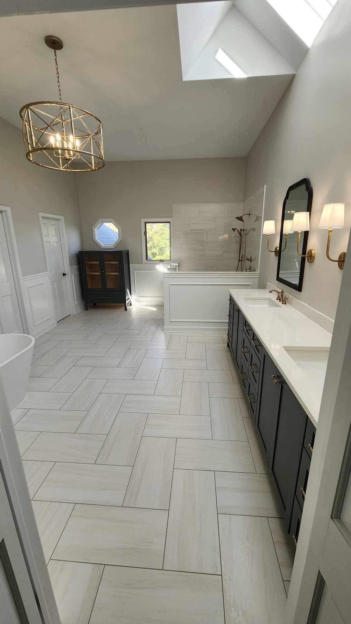 Bright modern bathroom with skylight, white tile floor, gray vanity, and tub alcove.
