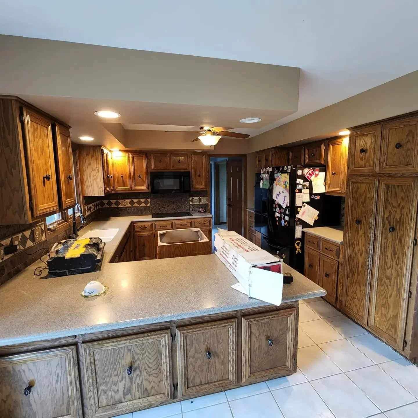 Spacious kitchen with wood cabinets, large island, tiled floor, and black appliances.