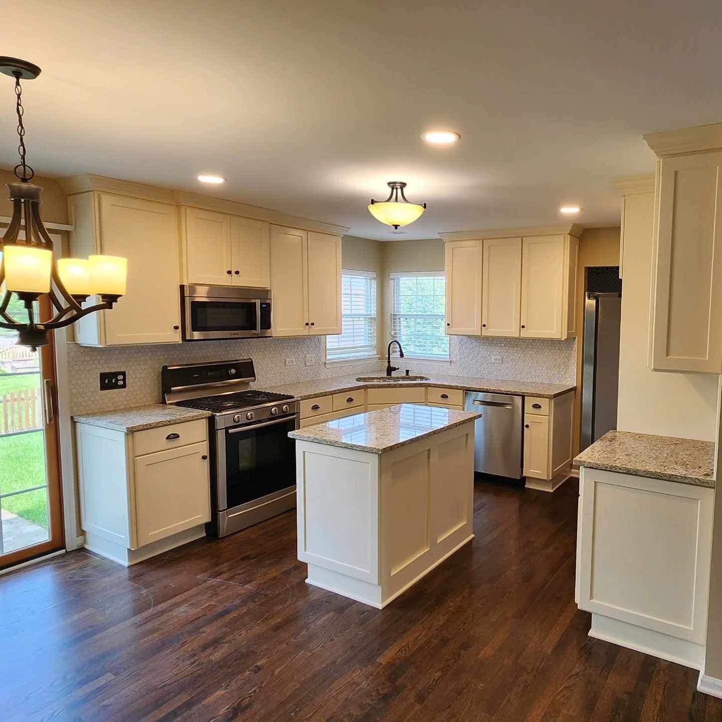 Bright modern kitchen with granite counters, white cabinets, island, and wood floors
