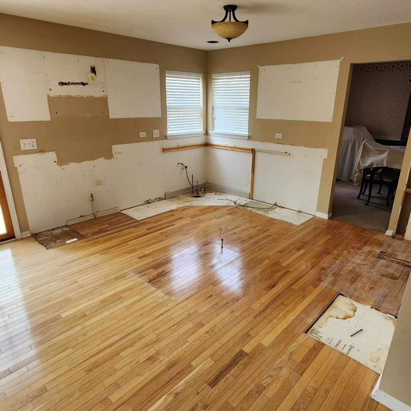 Empty room with hardwood floor, beige walls, windows, and signs of renovation work.