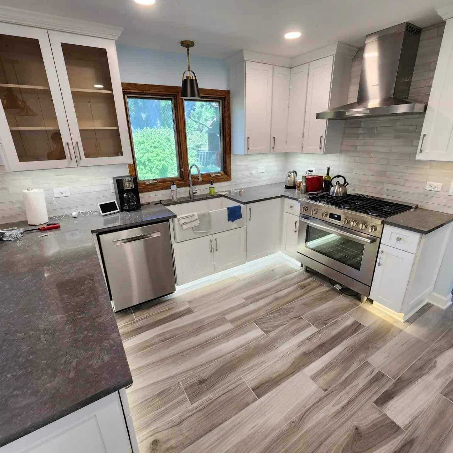 Bright modern kitchen with white cabinets, stainless appliances, gray countertops, and wood-look flooring.