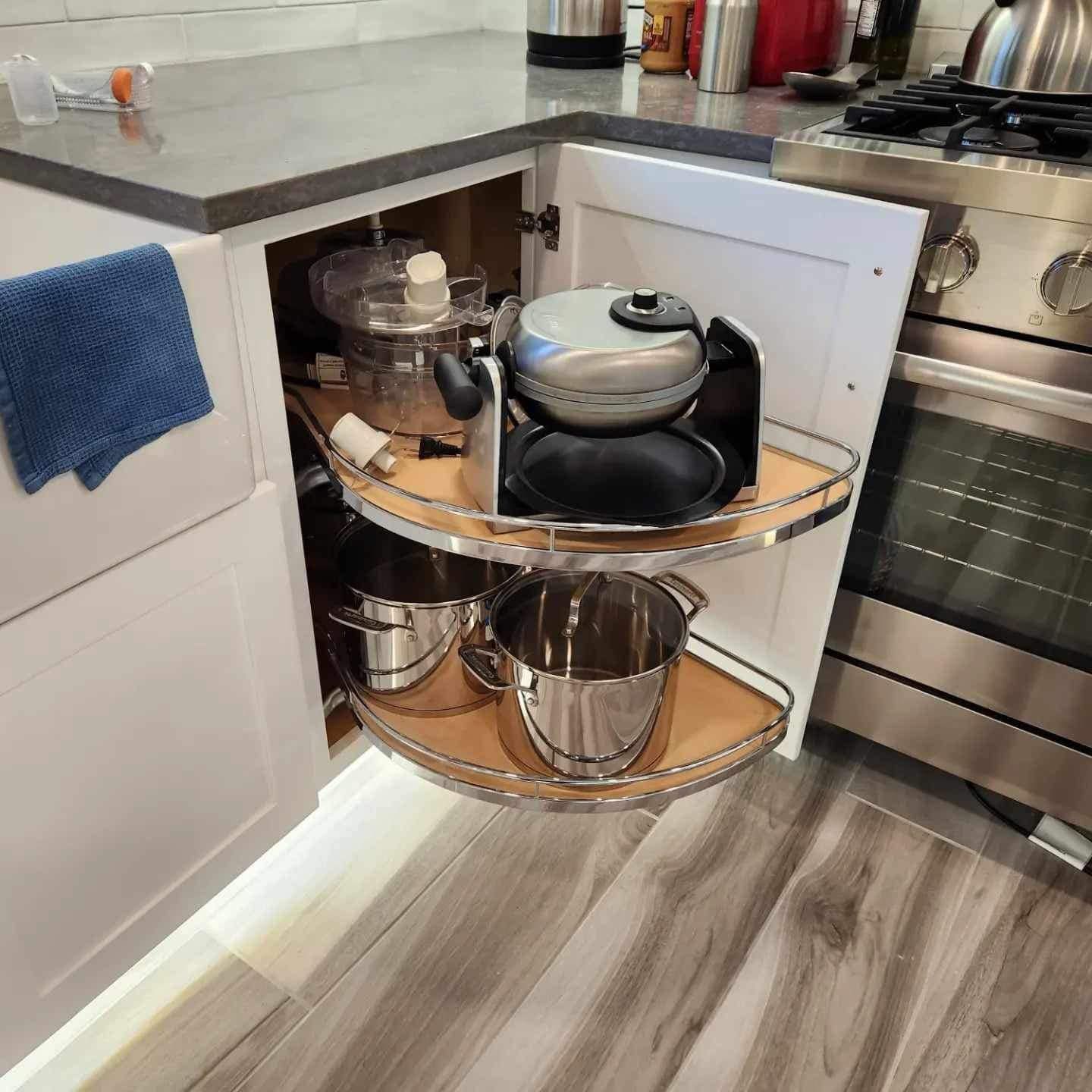 Kitchen corner with open pull-out shelves holding pots, pans, and a kettle under the countertop.