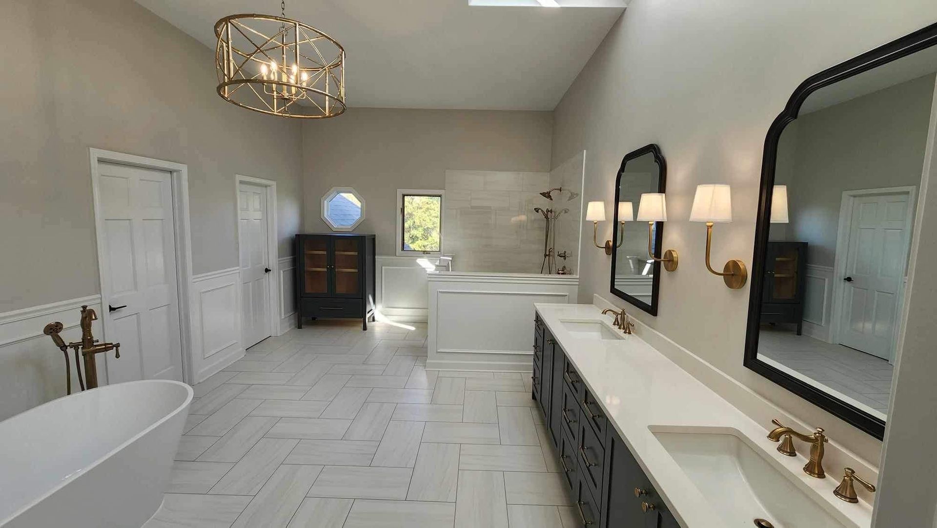 Bright modern bathroom with freestanding tub, double vanity, large mirrors, and gold fixtures.