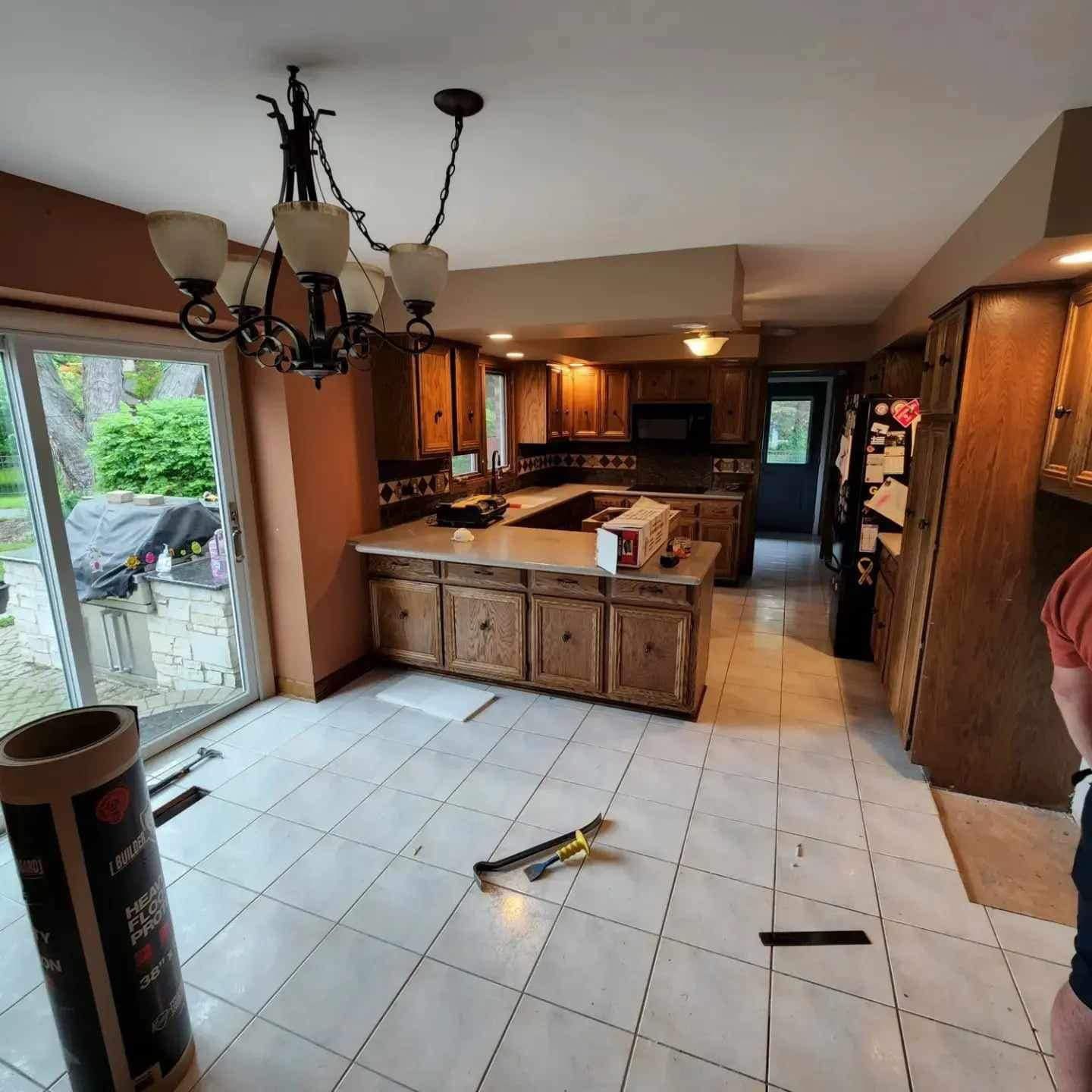 Kitchen with wood cabinets, island, chandelier, and tiled floor, with a sliding door opening to a backyard.