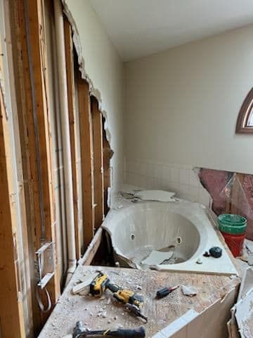 Bathroom under renovation with exposed studs, a white sink, tools, and debris on a dusty counter