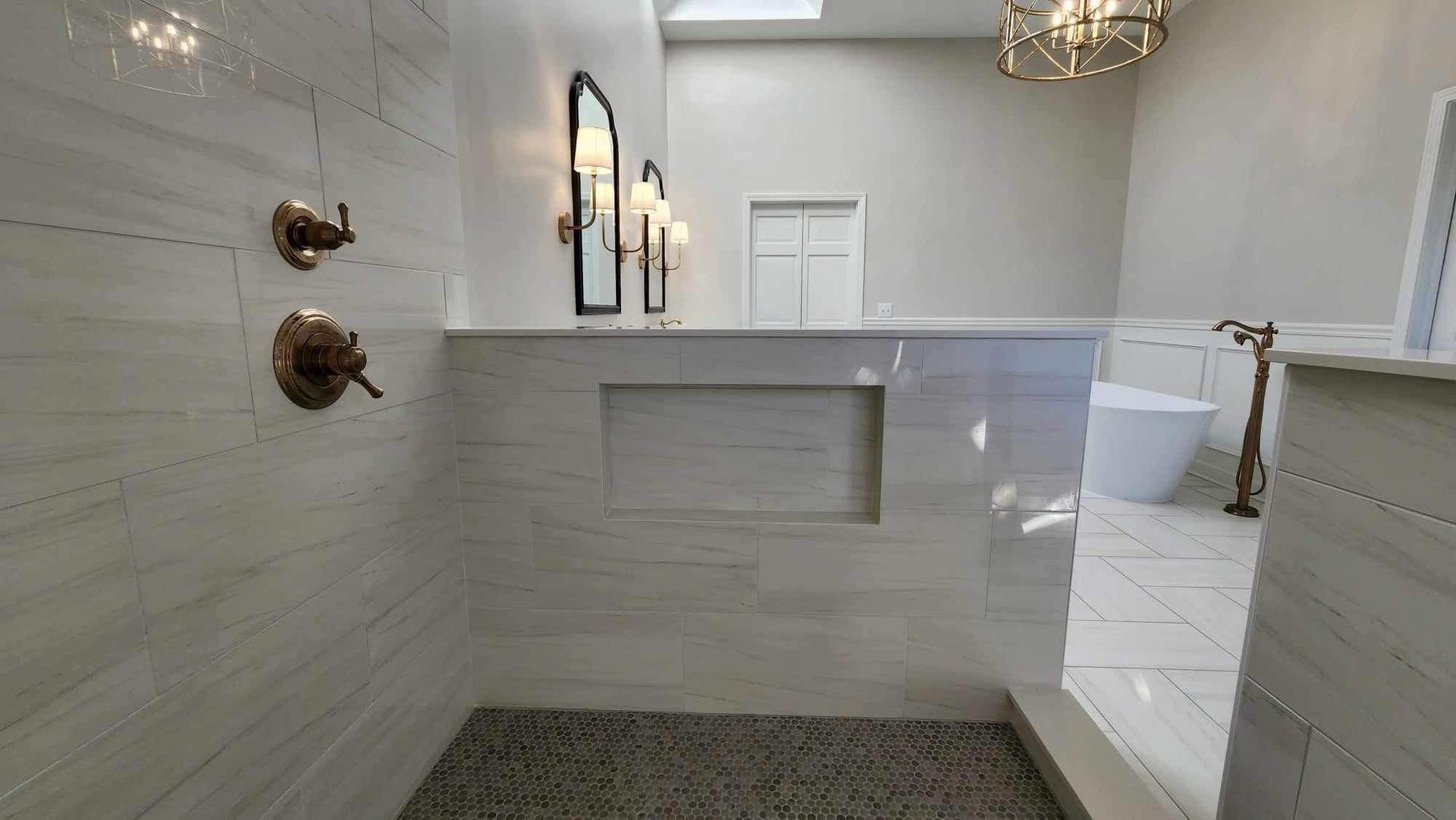 Modern white bathroom with walk-in shower, freestanding tub, and dark pebble floor.