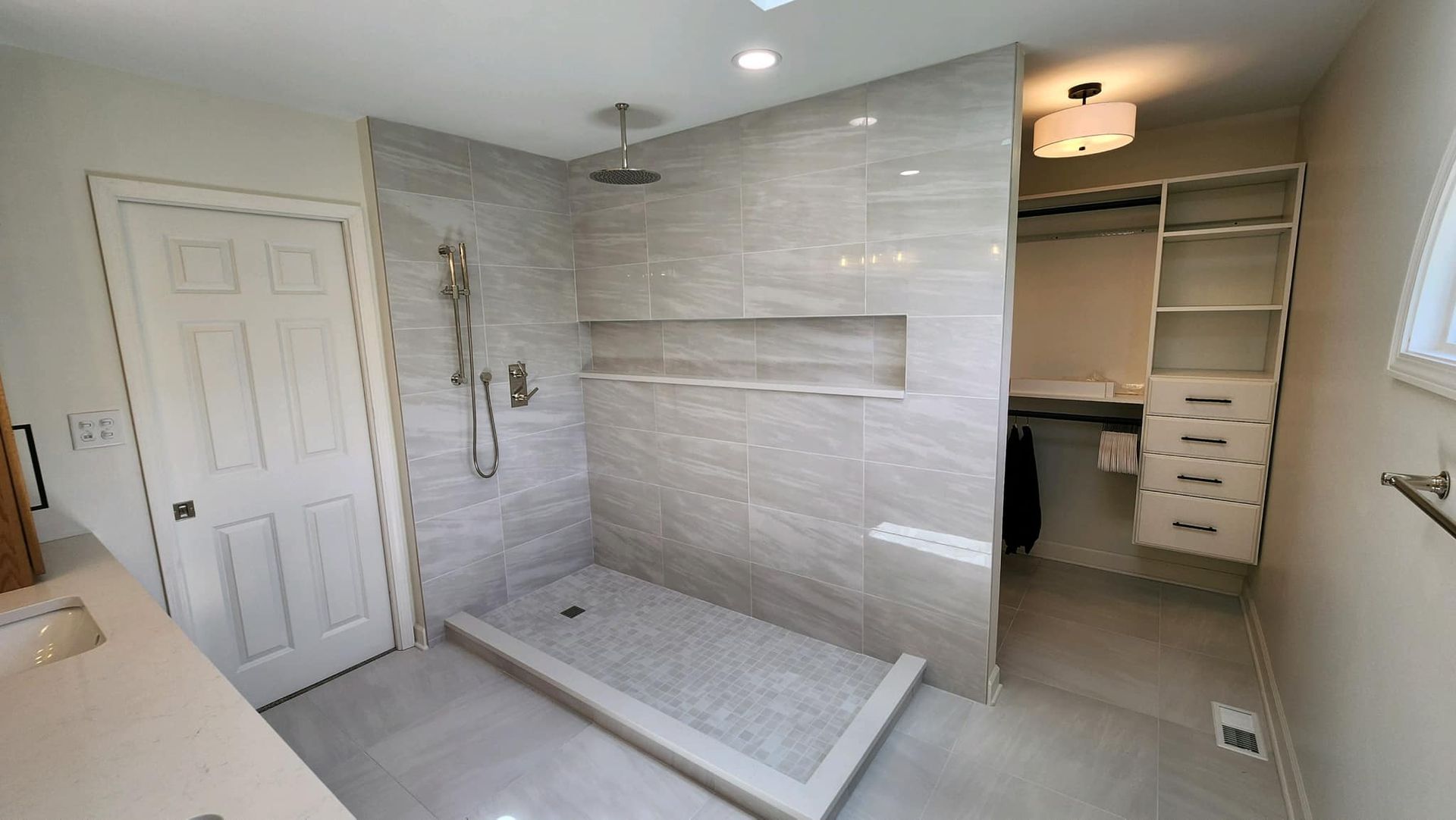 Modern bathroom with tiled walk-in shower, bench, and adjacent vanity area