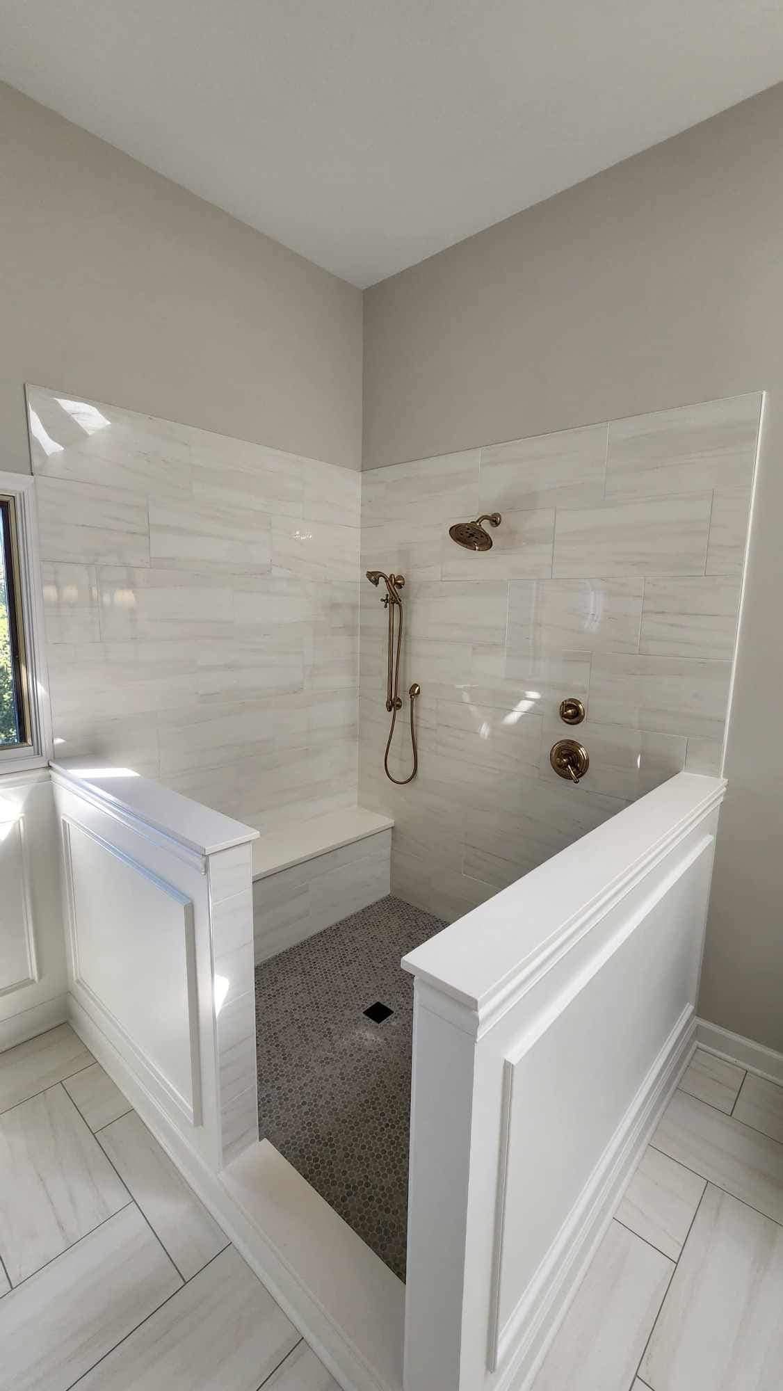 White-tiled shower with black mosaic floor and half walls in a bright bathroom.