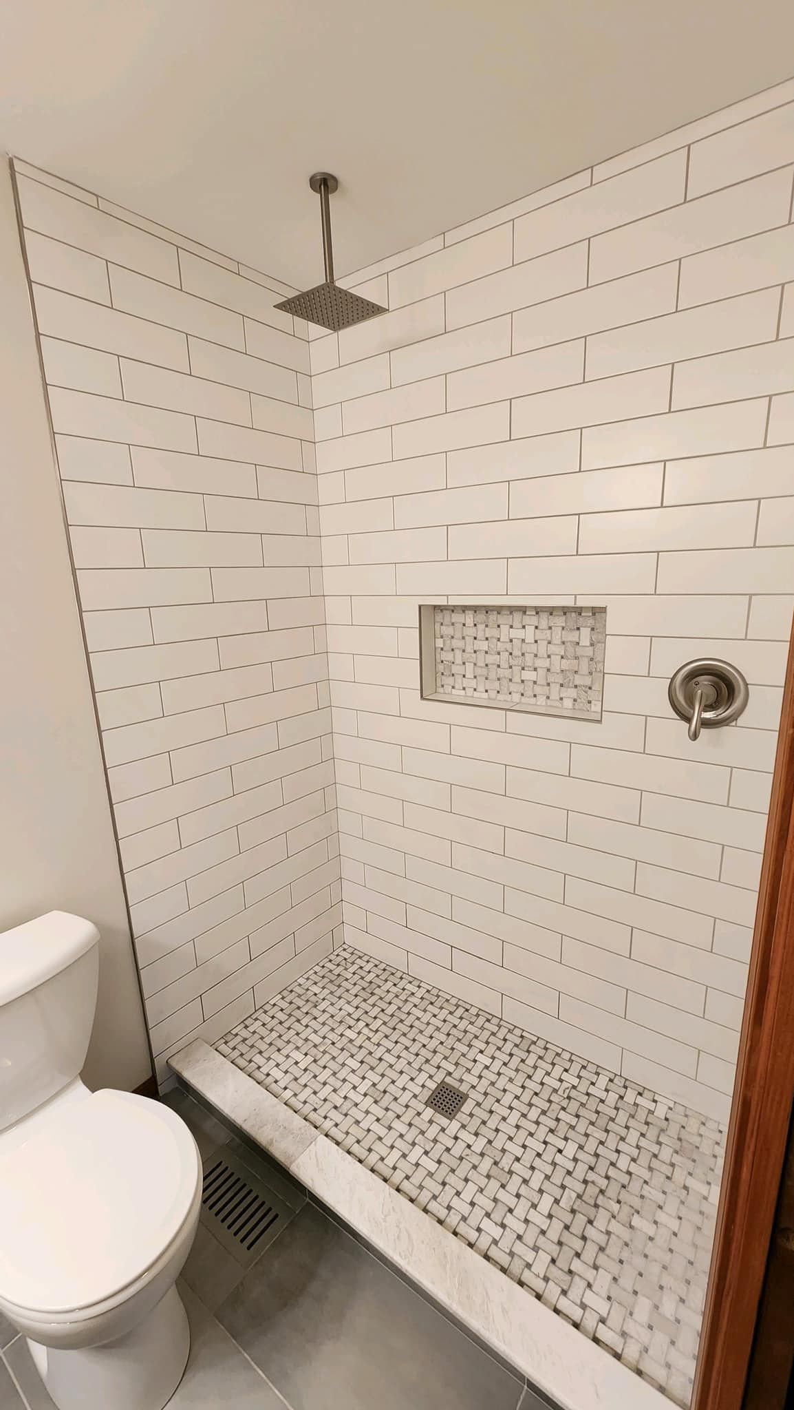 Small white-tiled bathroom shower with a built-in niche and overhead showerhead, beside a toilet.