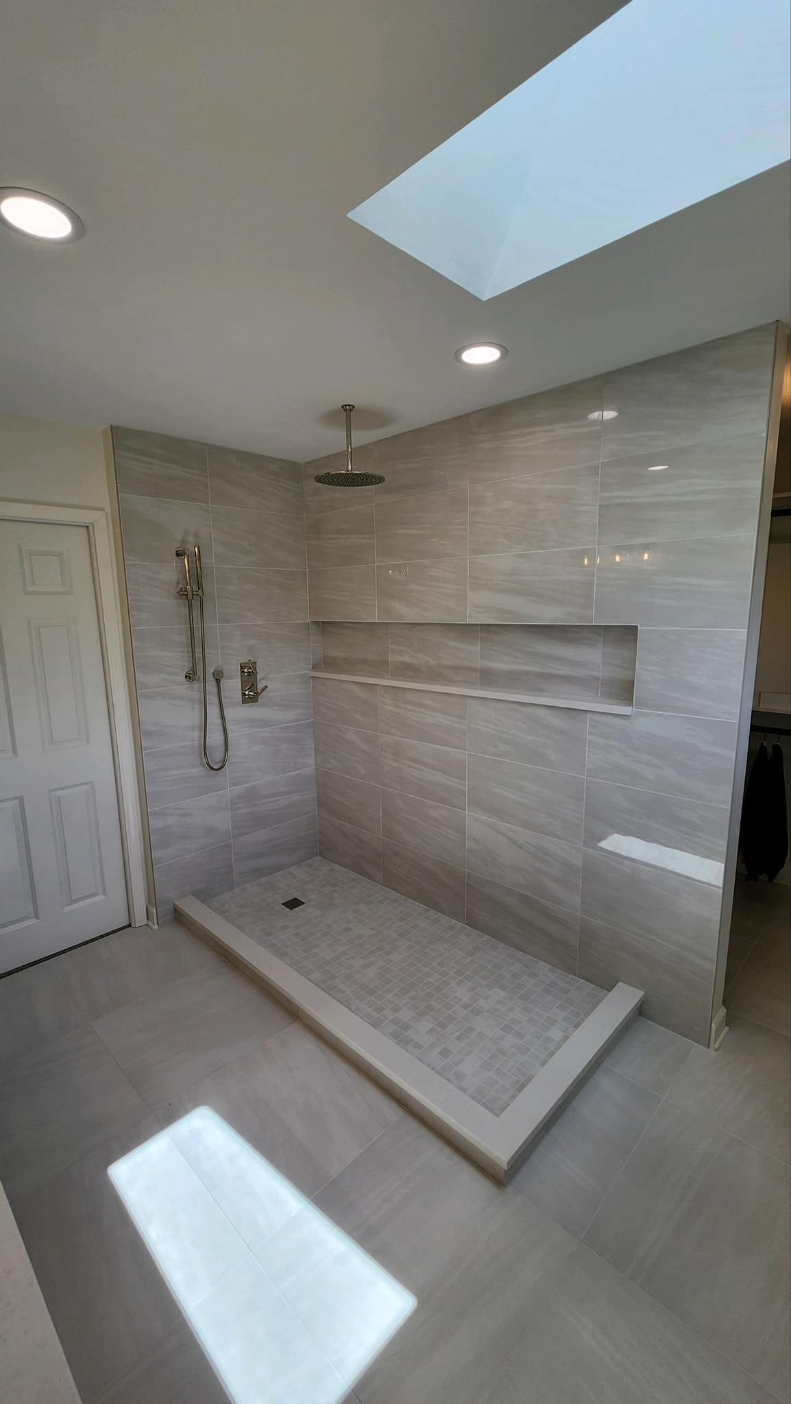 Modern tiled walk-in shower with skylight, bench, and built-in shelf in a bright bathroom