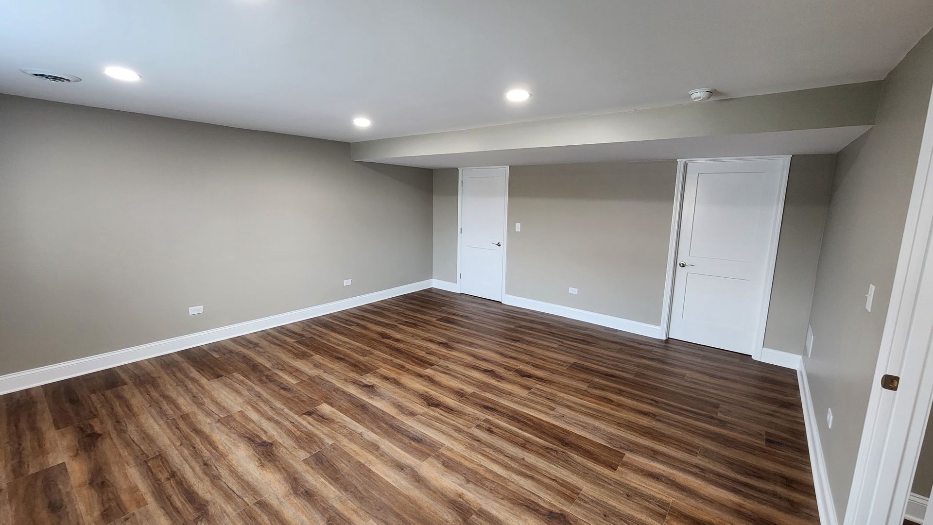 Empty beige room with wood flooring, recessed lights, and two white doors