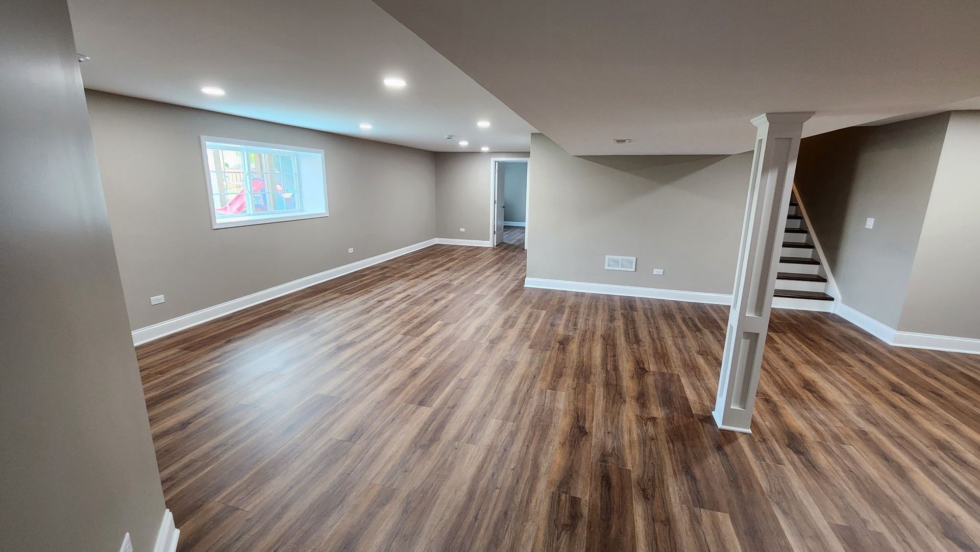 Empty finished basement with wood floors, gray walls, staircase, and recessed lighting.
