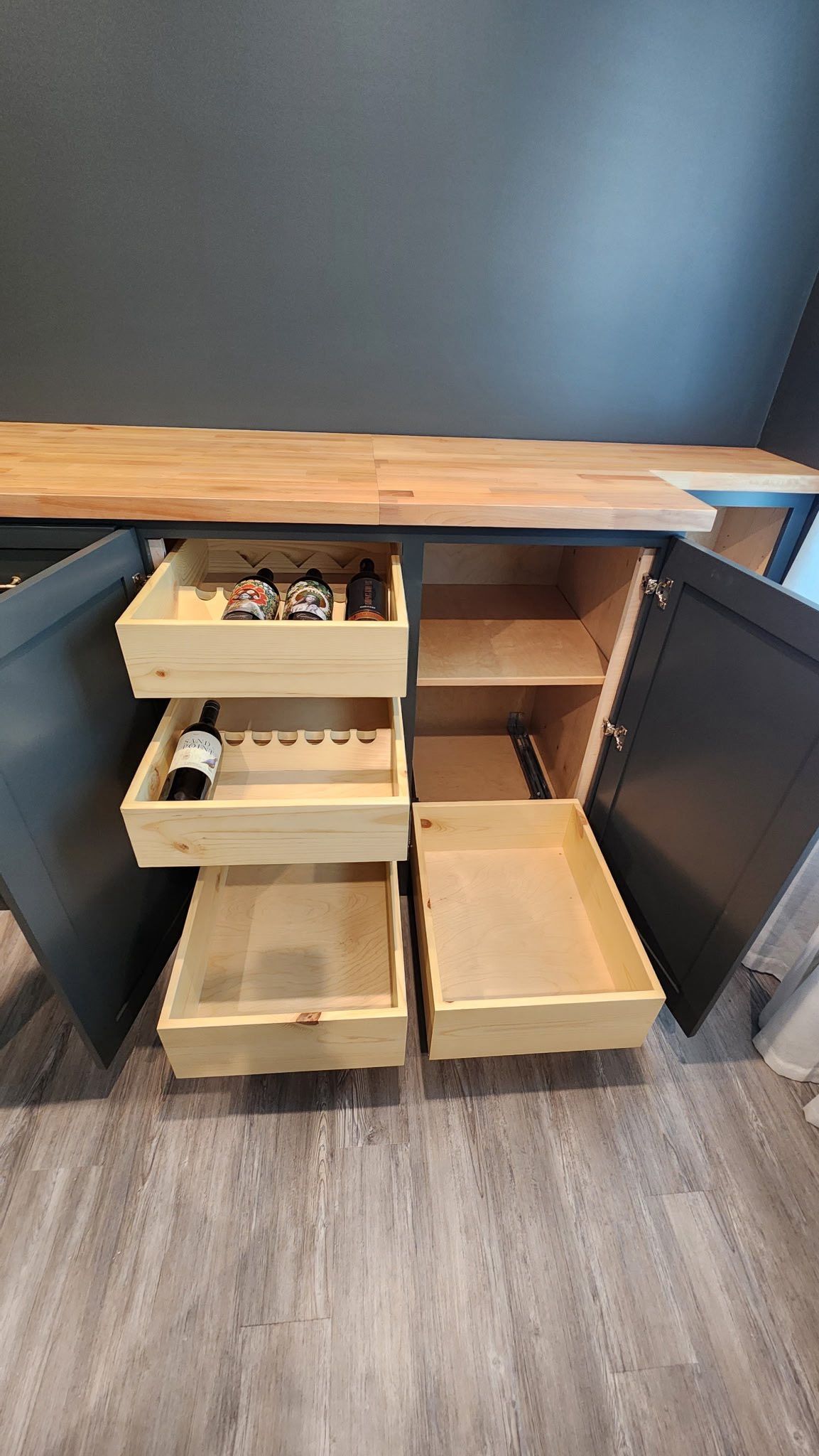 Open kitchen cabinet with pull-out drawers and wood countertops against a dark wall.