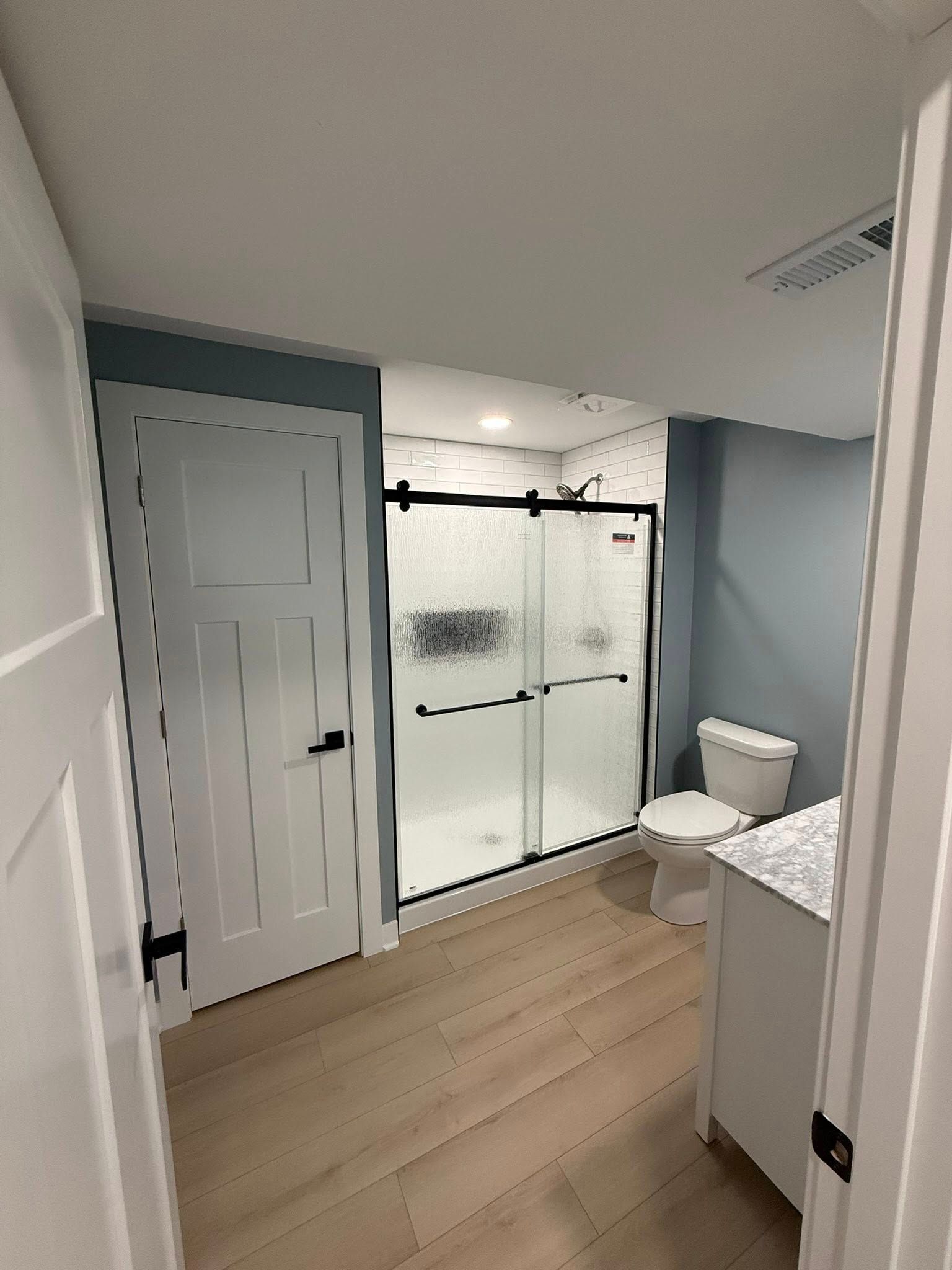 Bathroom with glass shower, toilet, vanity, and light wood floor in a blue-gray room