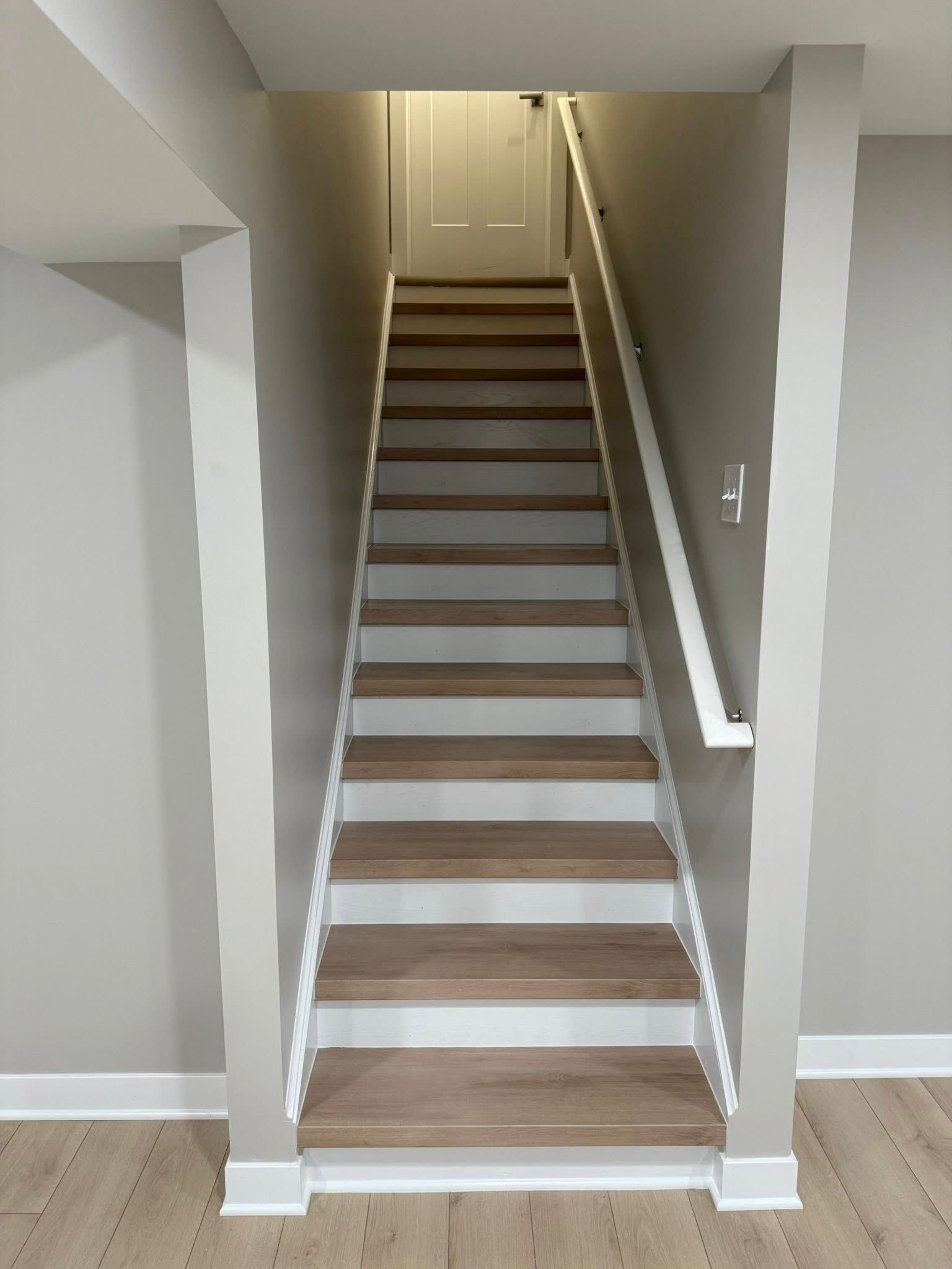 Narrow indoor staircase with brown steps, white railings, and a closed door at the top