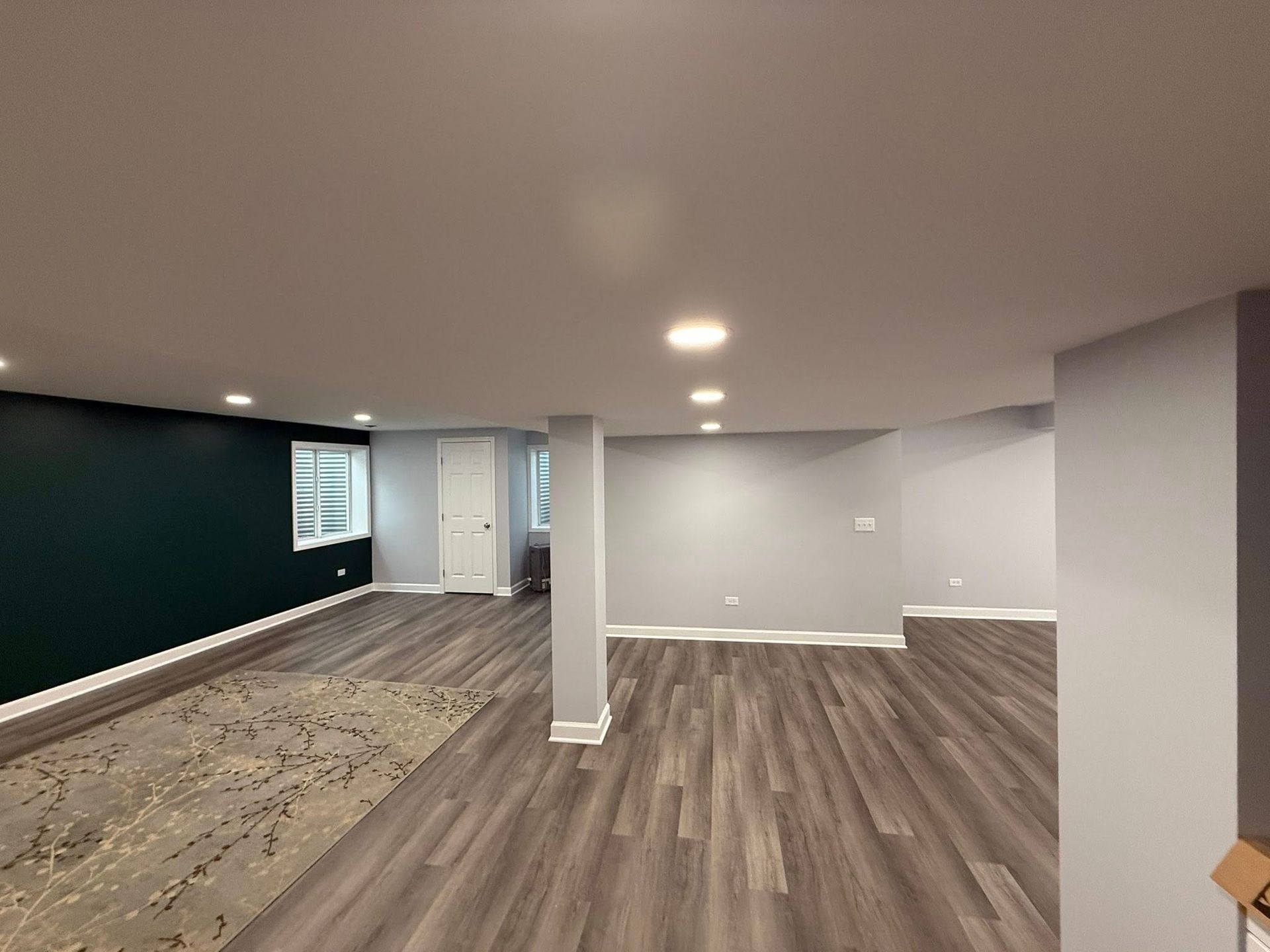 Empty finished basement with wood floors, gray walls, white columns, and a dark teal accent wall.