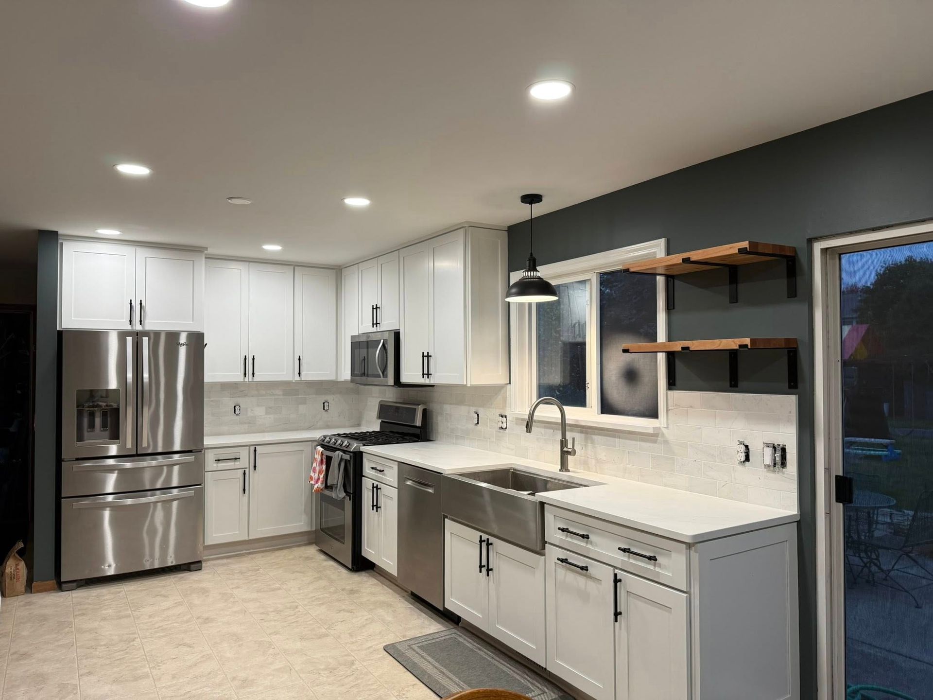 Modern kitchen with white cabinets, stainless steel appliances, gray countertops, and open wood shelves
