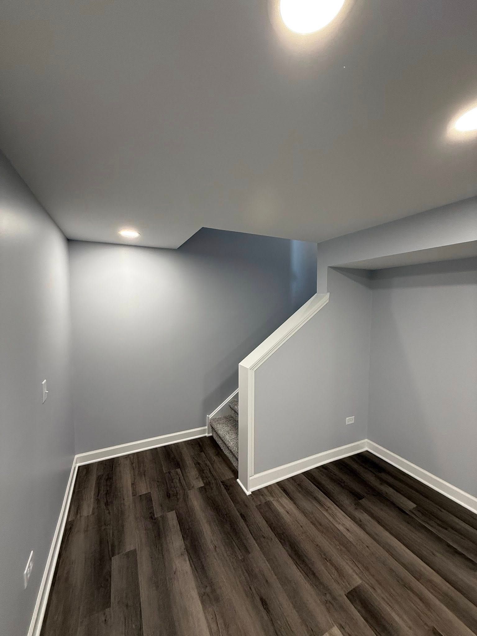 Empty gray room with dark wood floors and a stairway opening under a sloped ceiling
