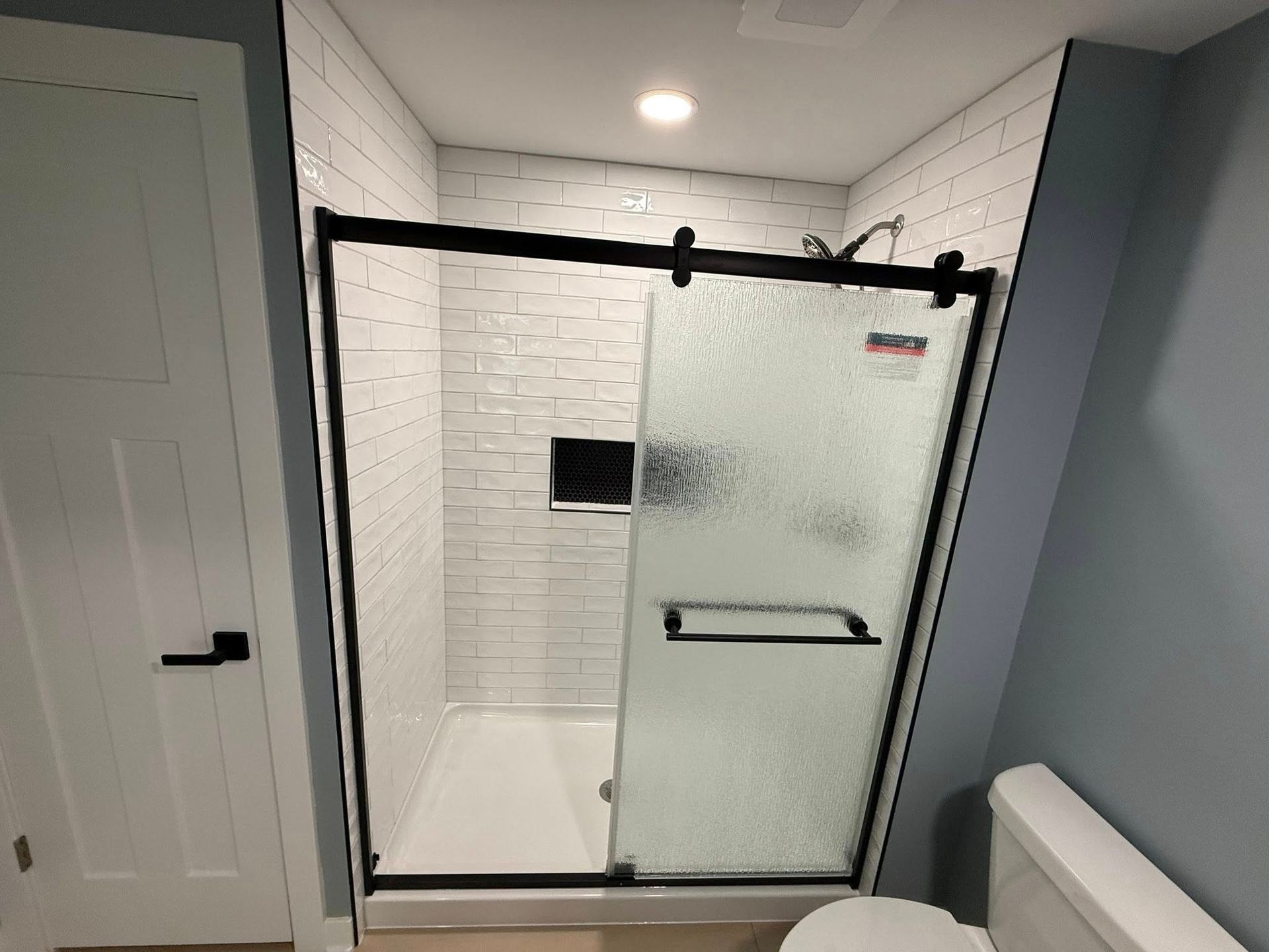 Modern bathroom with a glass shower enclosure, white tile walls, and a gray vanity edge.
