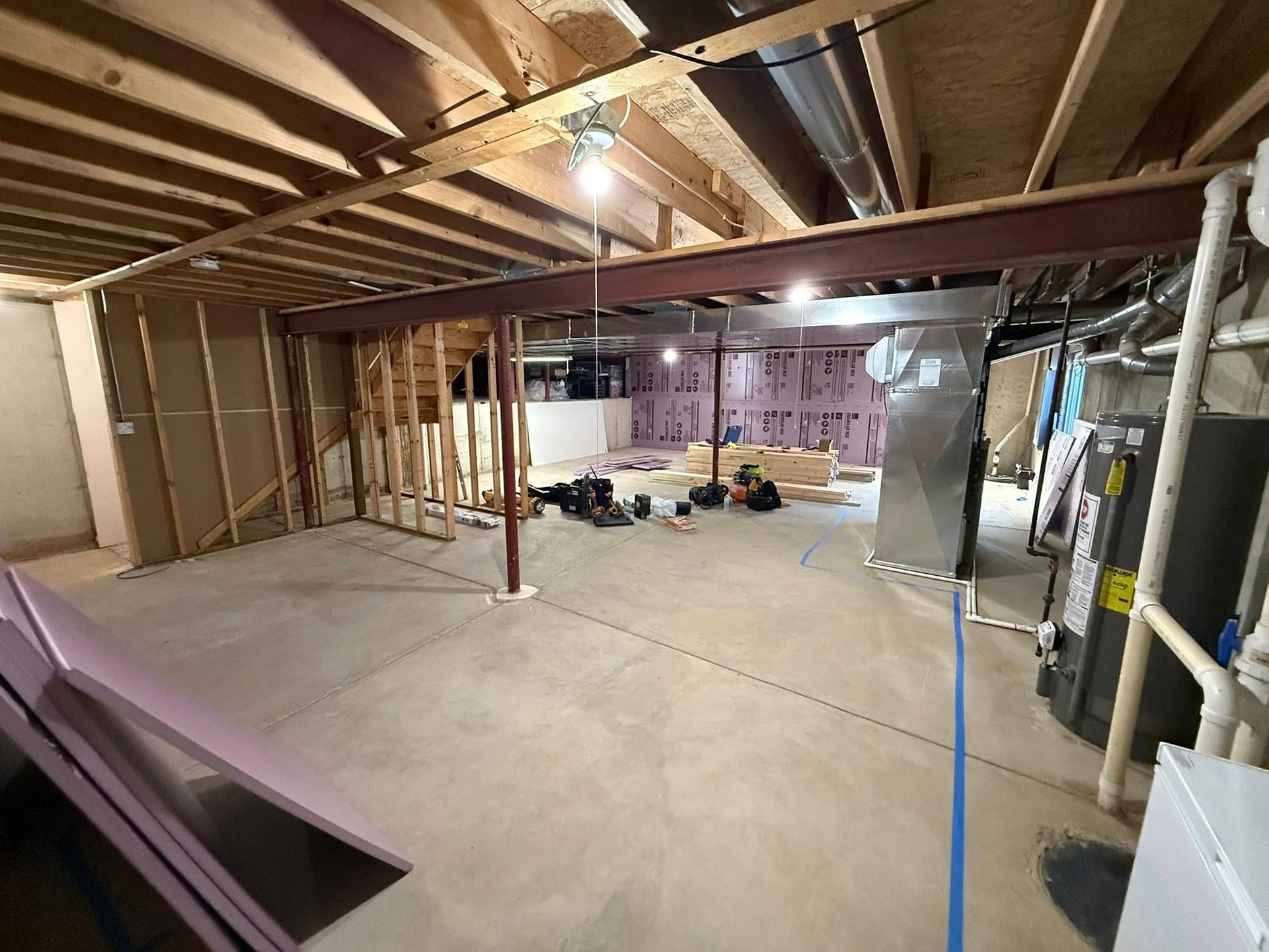 Unfinished basement with exposed beams, concrete floor, and scattered construction materials.