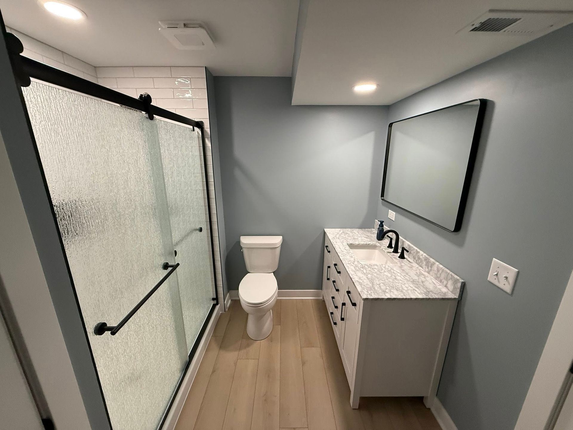 Modern bathroom with shower, toilet, vanity sink, and wall mirror in gray and white tones